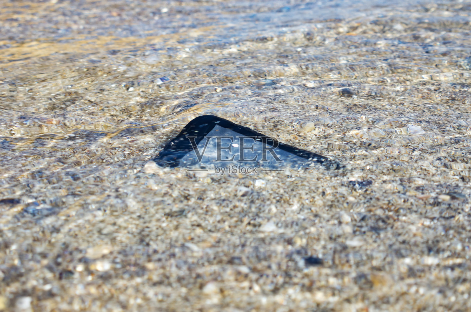 度假时在海边丢了智能手机。寻找丢失的东西，修复溺亡的手机，概念形象。照片摄影图片