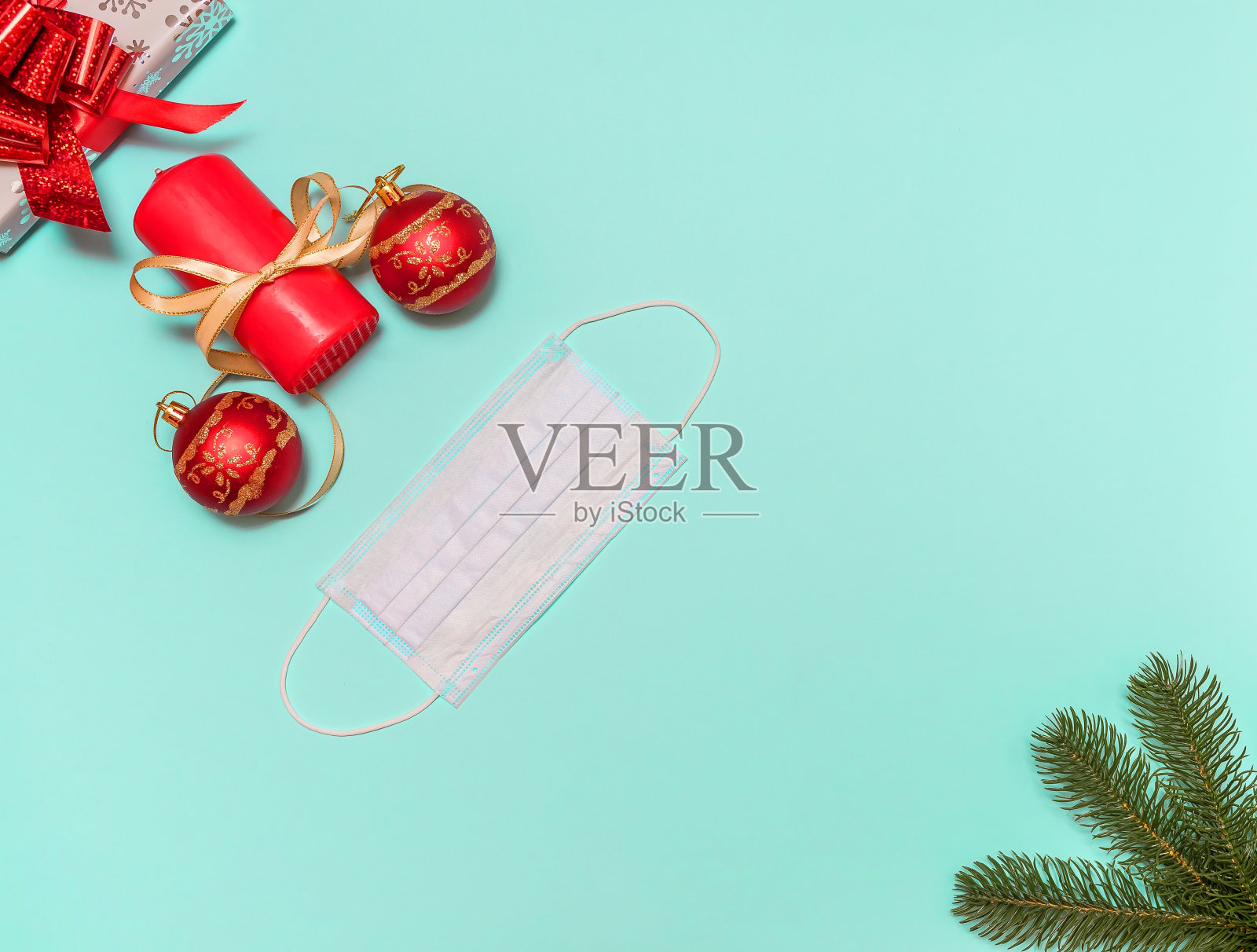 新年装饰以蓝色为底色，配上一份礼物和一支红烛。面具保护。圣诞树枝。照片摄影图片