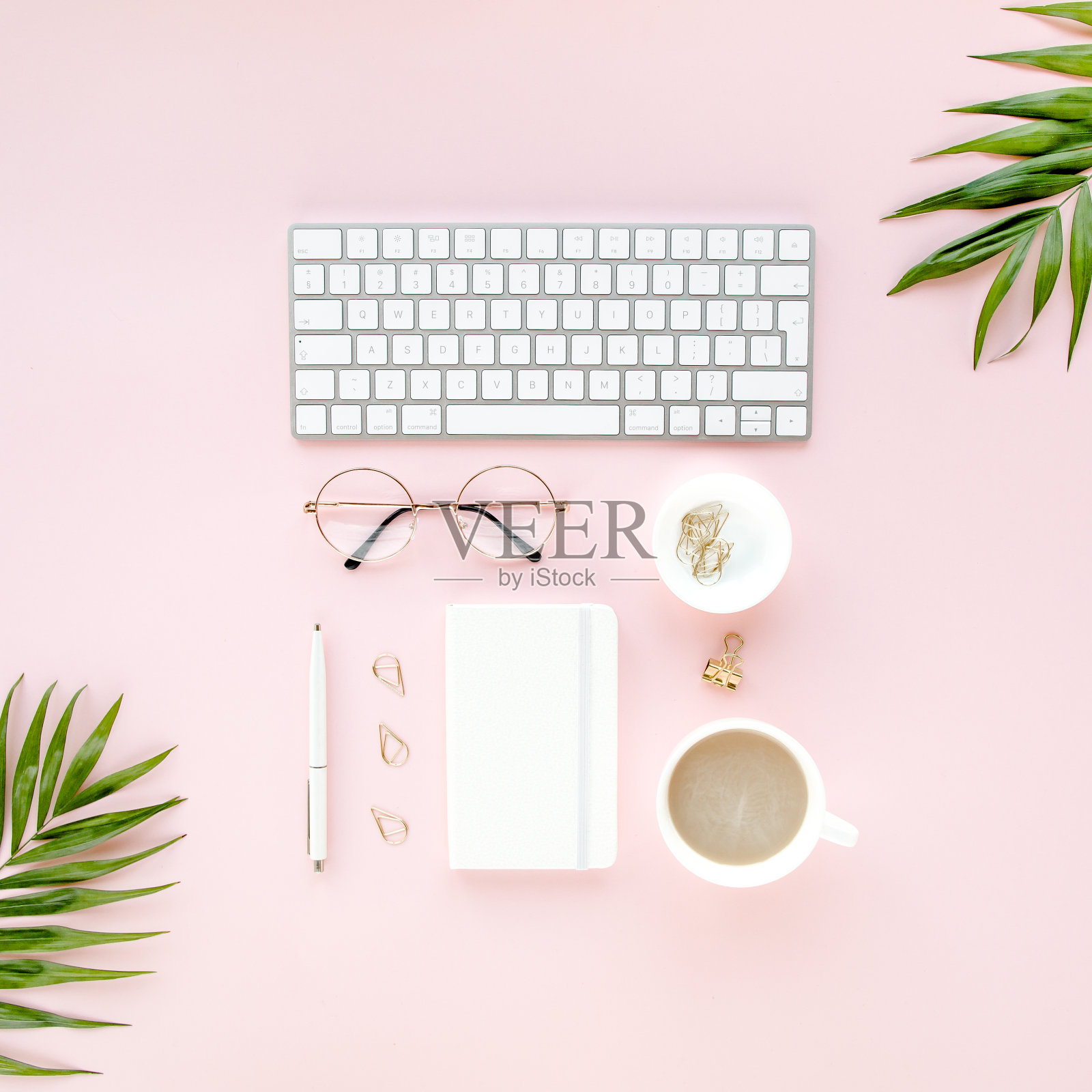 办公桌上有电脑书桌，绿叶手掌，剪贴板。前视图。平的。家庭办公空间。粉色背景上的女性配饰照片摄影图片