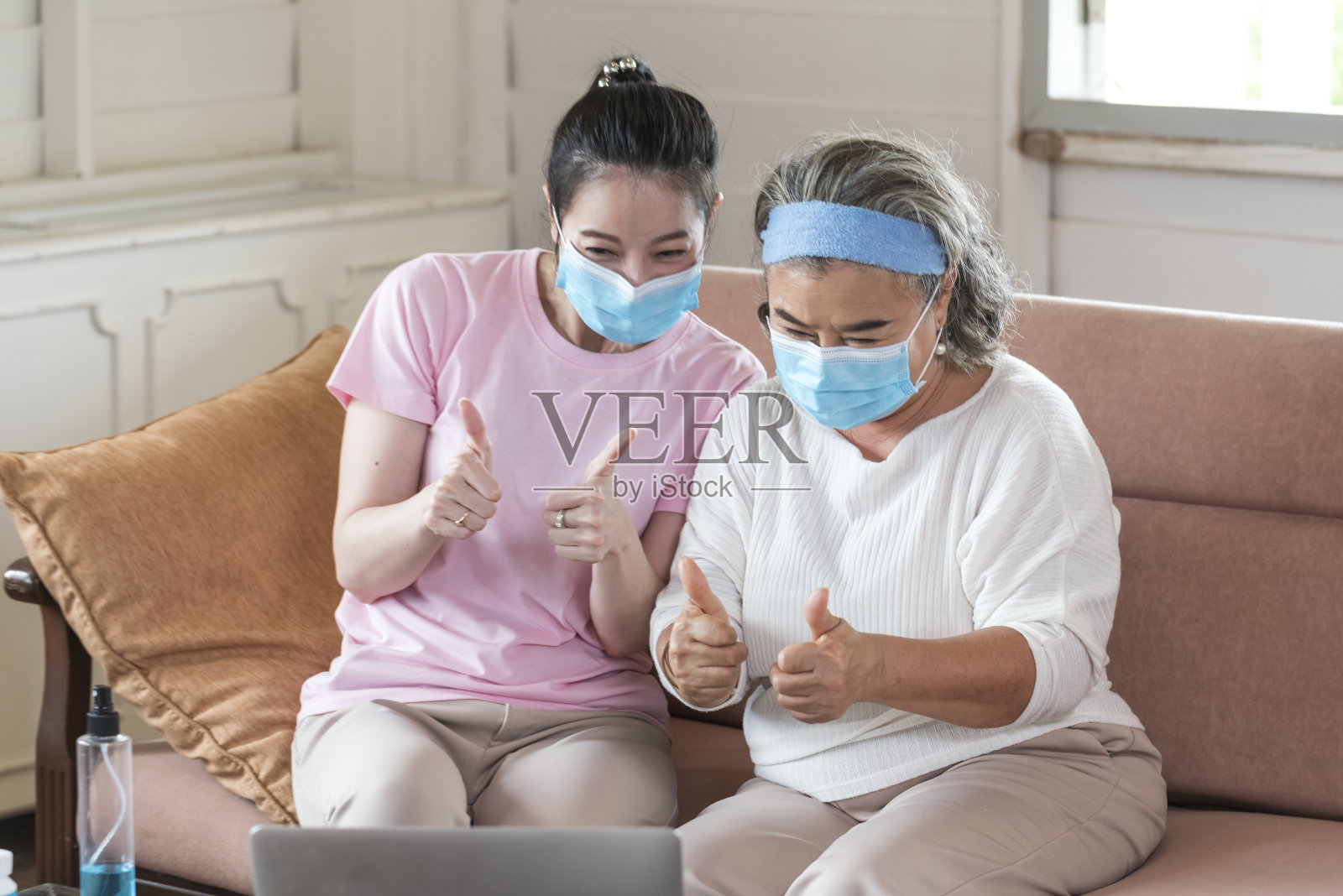 亚洲年轻女子教年长的母亲，如何戴口罩从网上学习在客厅仔细。家庭的概念照片摄影图片