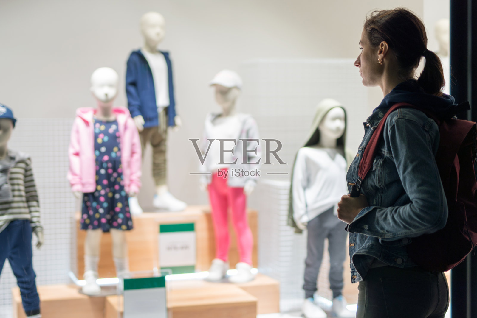 一位妇女站在儿童商店外，看着模特身上的衣服。照片摄影图片