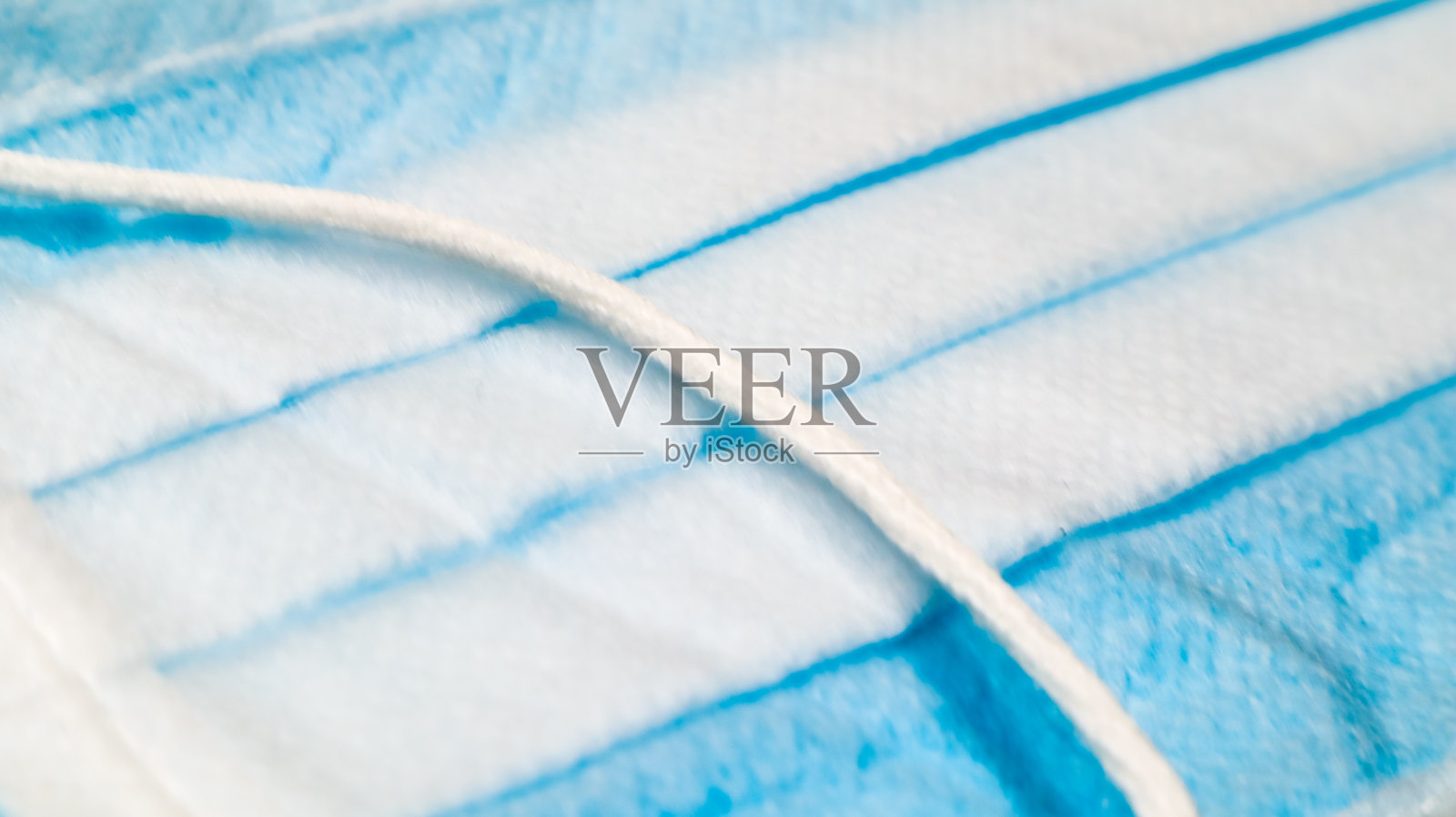 一个三层一次性外科口罩特写与橡胶垫覆盖嘴和鼻子在蓝色背景。防护细菌、保健和医药的概念。新型冠状病毒肺炎照片摄影图片