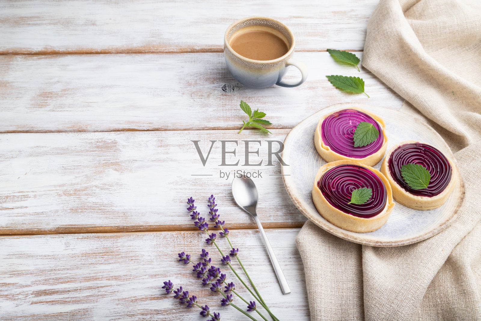 在白色的木质背景和亚麻织物上，配有果冻和牛奶奶油的甜馅饼和一杯咖啡。侧视图，拷贝空间。照片摄影图片