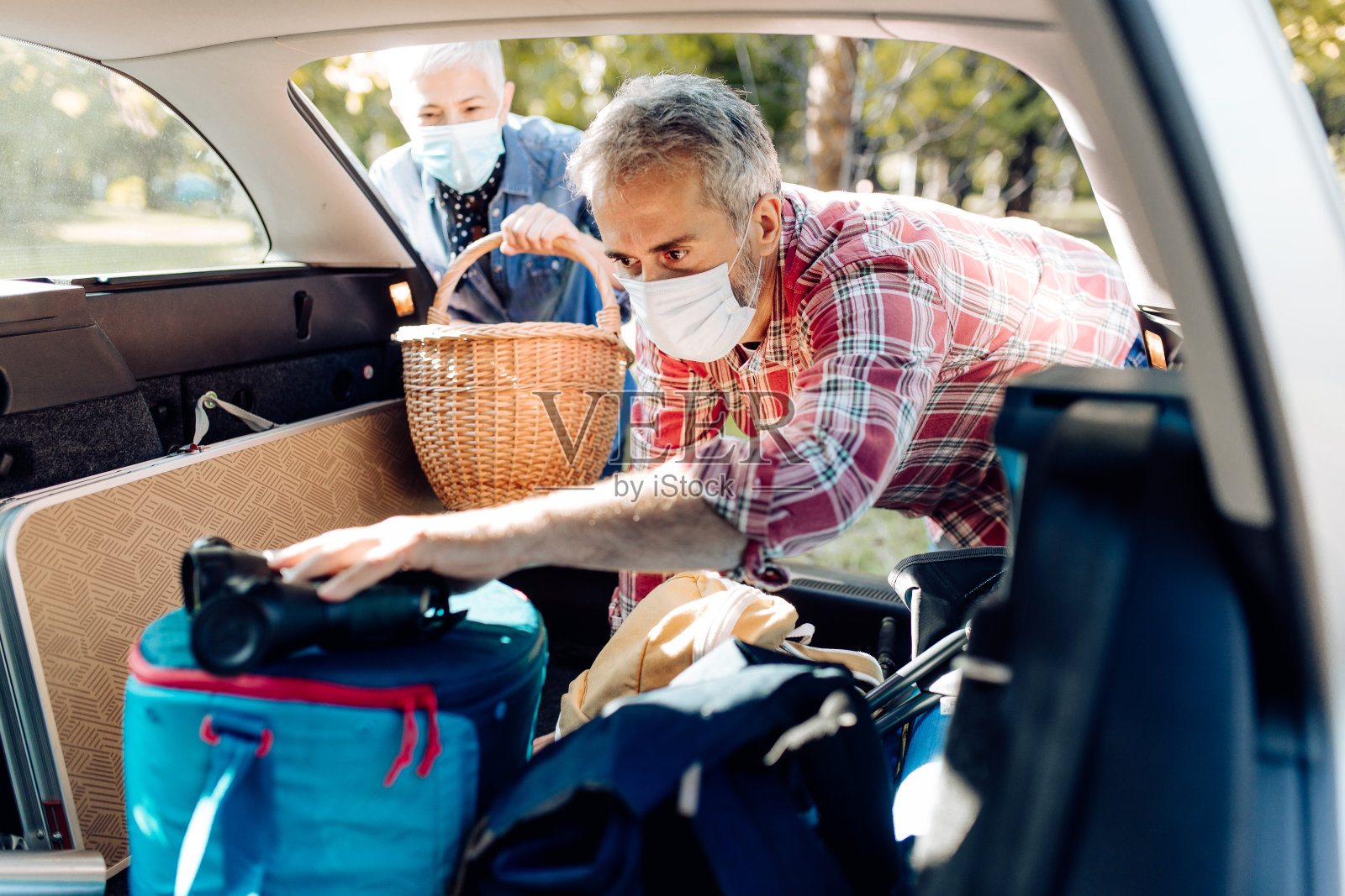 成熟的夫妇戴着口罩和打包设备进入汽车后备箱照片摄影图片