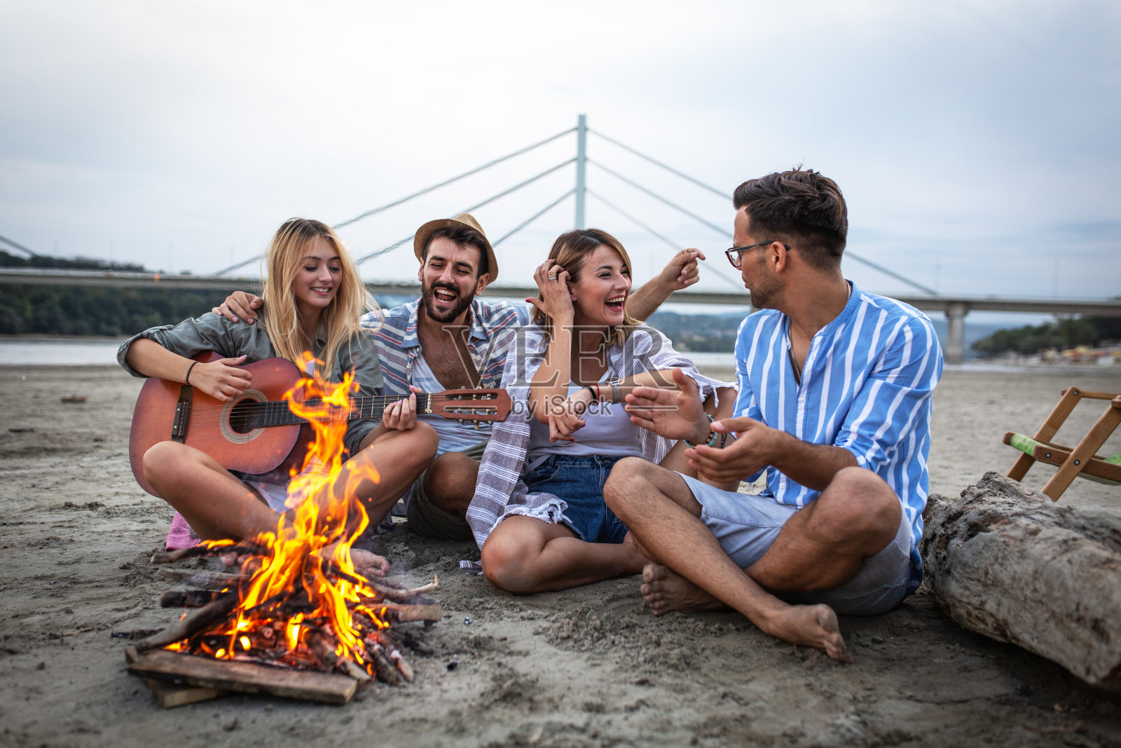 一群朋友坐在海滩上的篝火旁。照片摄影图片
