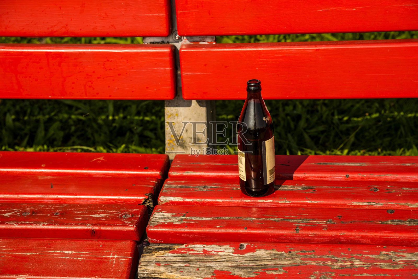 一个啤酒瓶放在公园的红色长凳上照片摄影图片
