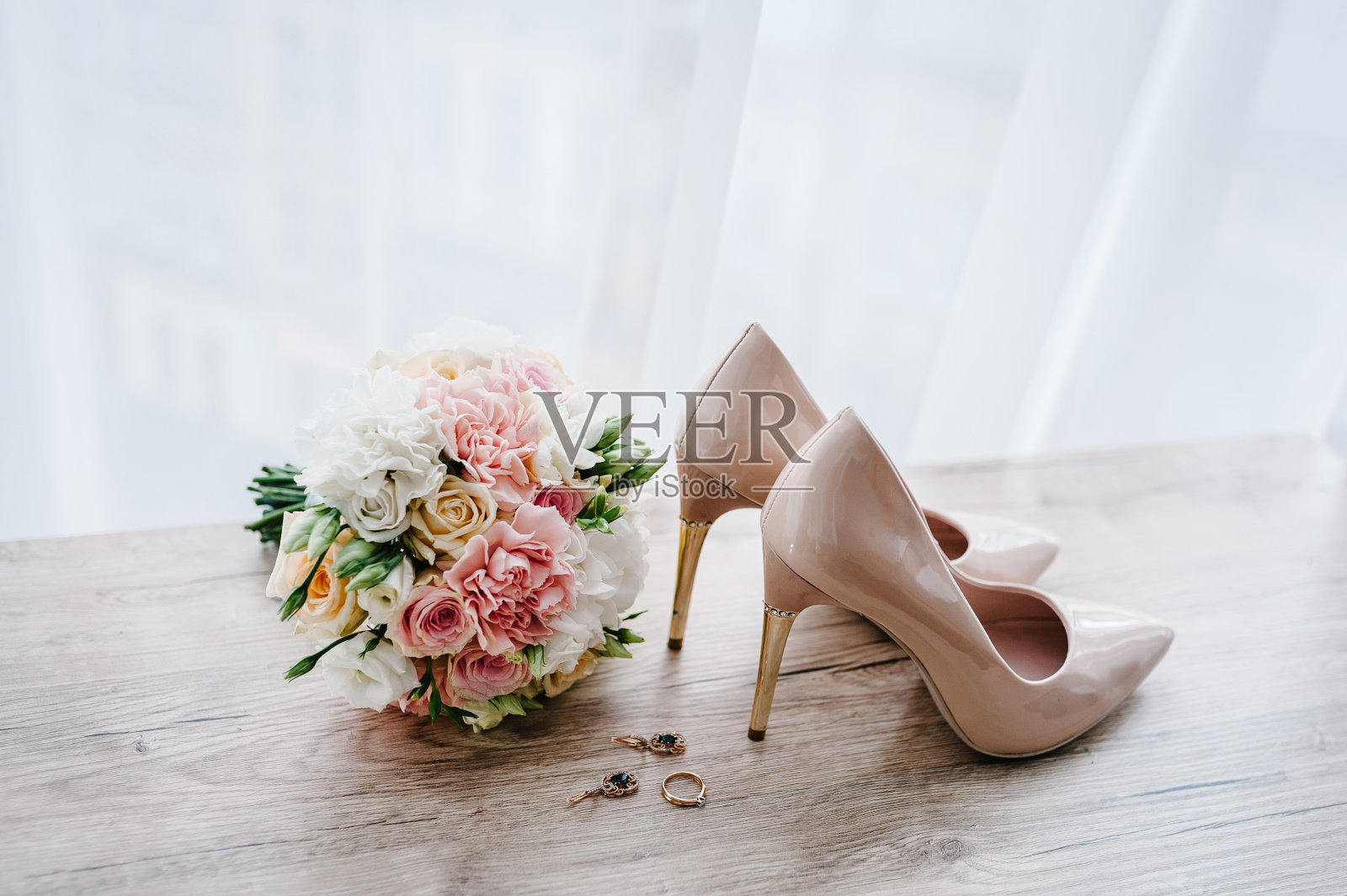 新娘的婚礼花束，粉色的玫瑰和绿色植物，时髦的经典漆米色鞋，耳环和戒指躺在木制的背景。新娘配件。关闭了。侧视图。照片摄影图片