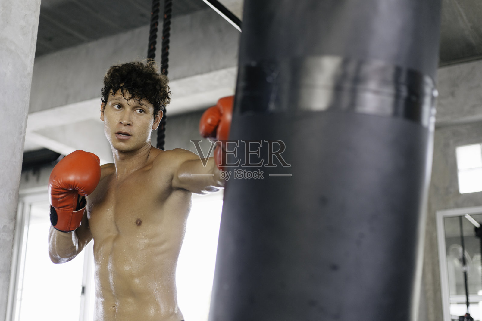 肖像年轻的白人肌肉强壮的男子在拳击手套训练锻炼在健身房健身。拳击手练习拳击袋拳。对抗运动照片摄影图片