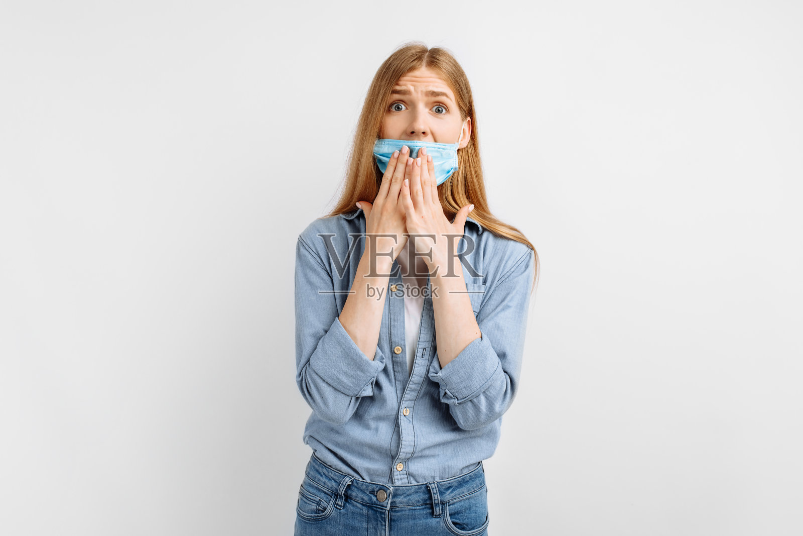震惊、诧异的年轻女子在脸上戴着医用防护口罩，诧异地用手捂着嘴，背景一片白茫茫照片摄影图片
