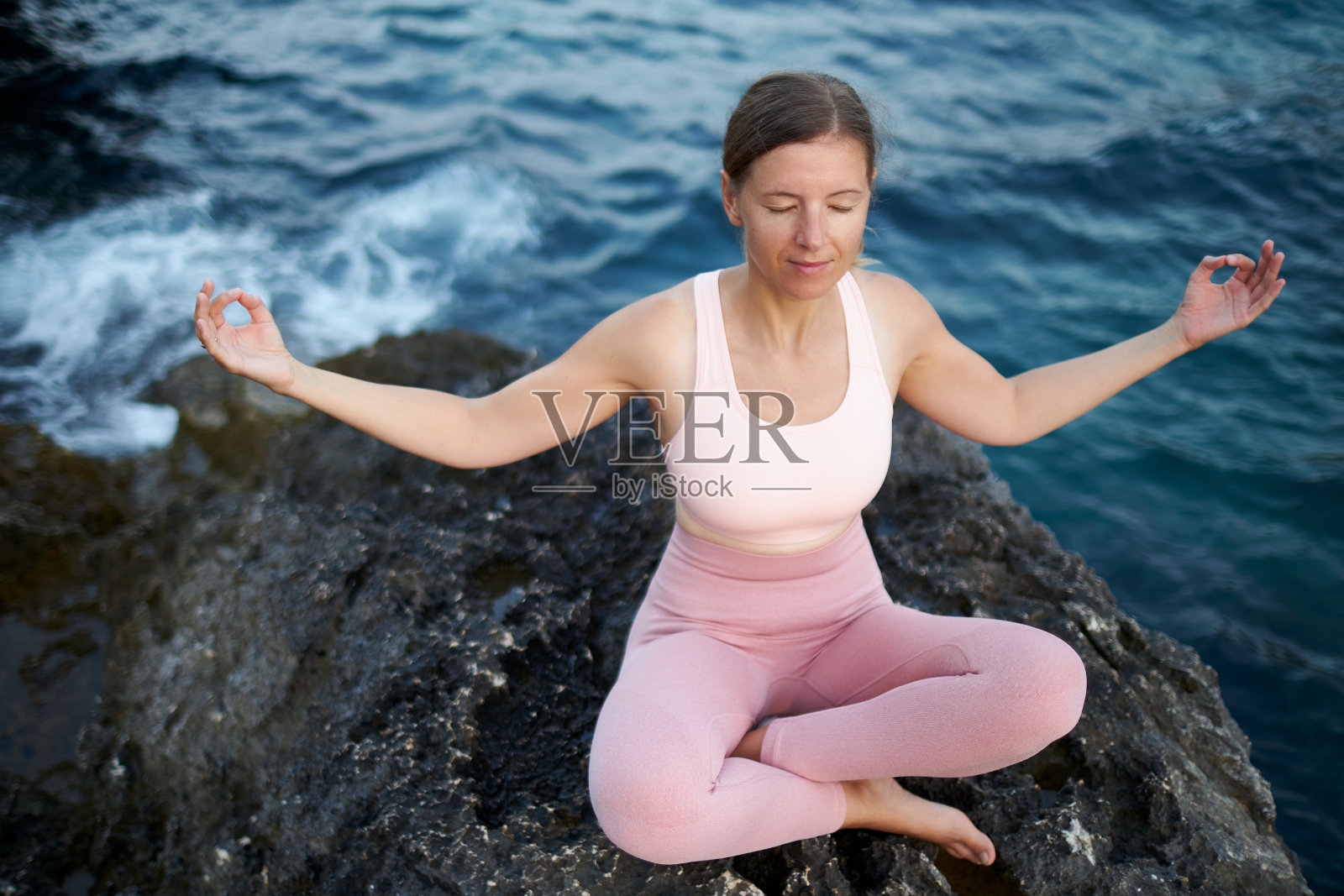 黄昏时分，一名三十多岁的女子在马略卡岛海边的岩石景观中做各种冥想和瑜伽练习照片摄影图片