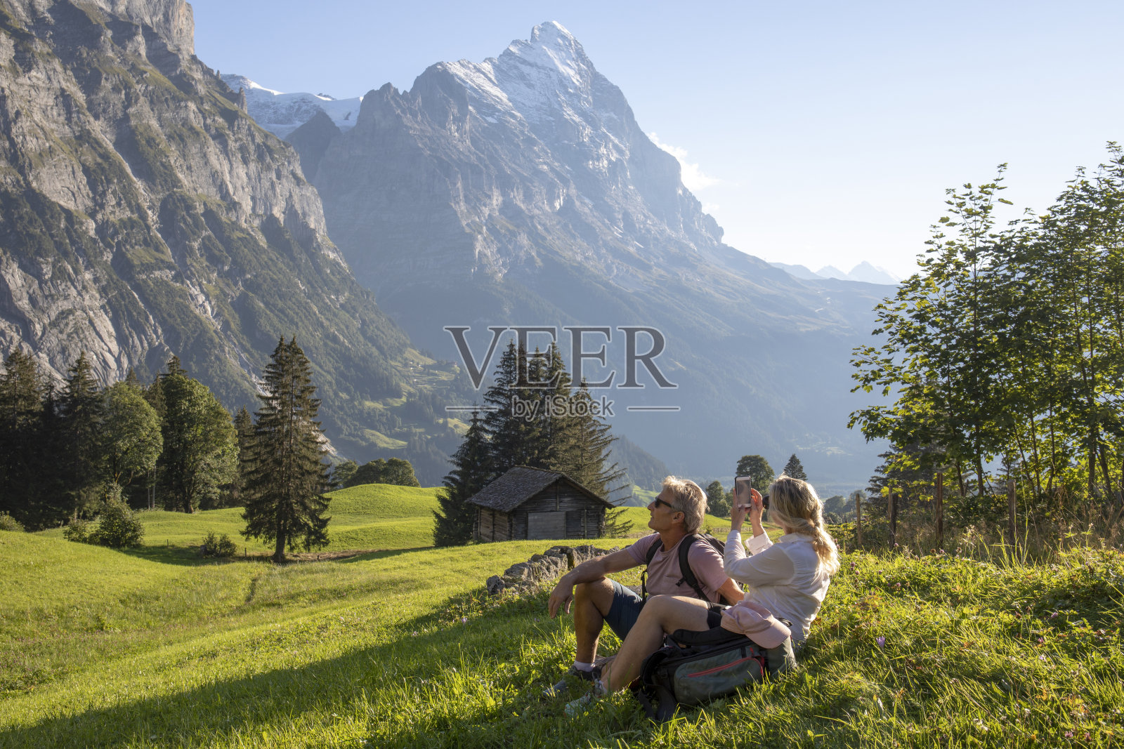 日出时分，徒步旅行的情侣们在高山草地上休息照片摄影图片