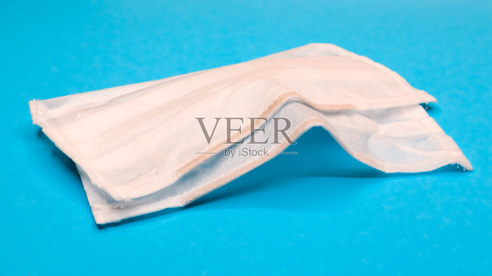 两个三层一次性外科口罩，用橡胶垫盖住口鼻，以蓝色背景。防护细菌、保健和医药的概念。新型冠状病毒肺炎照片摄影图片