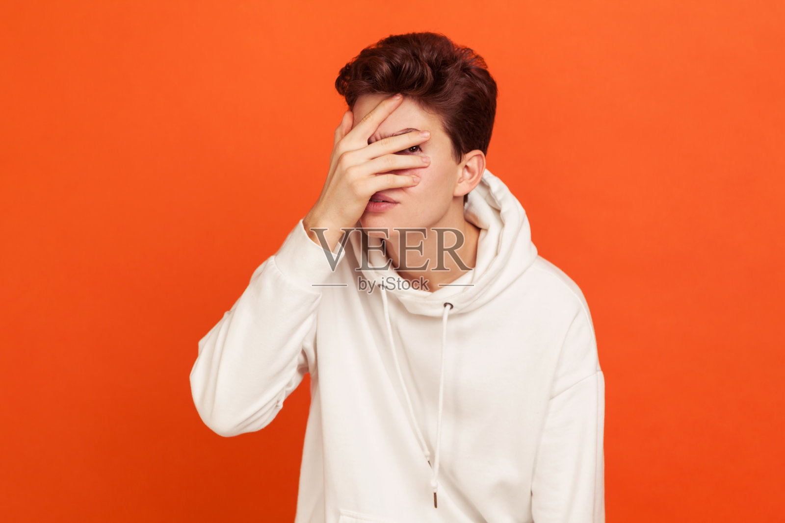 好奇的年轻人在休闲运动衫与兜帽看透过手指，害怕的青少年看与恐惧，间谍照片摄影图片