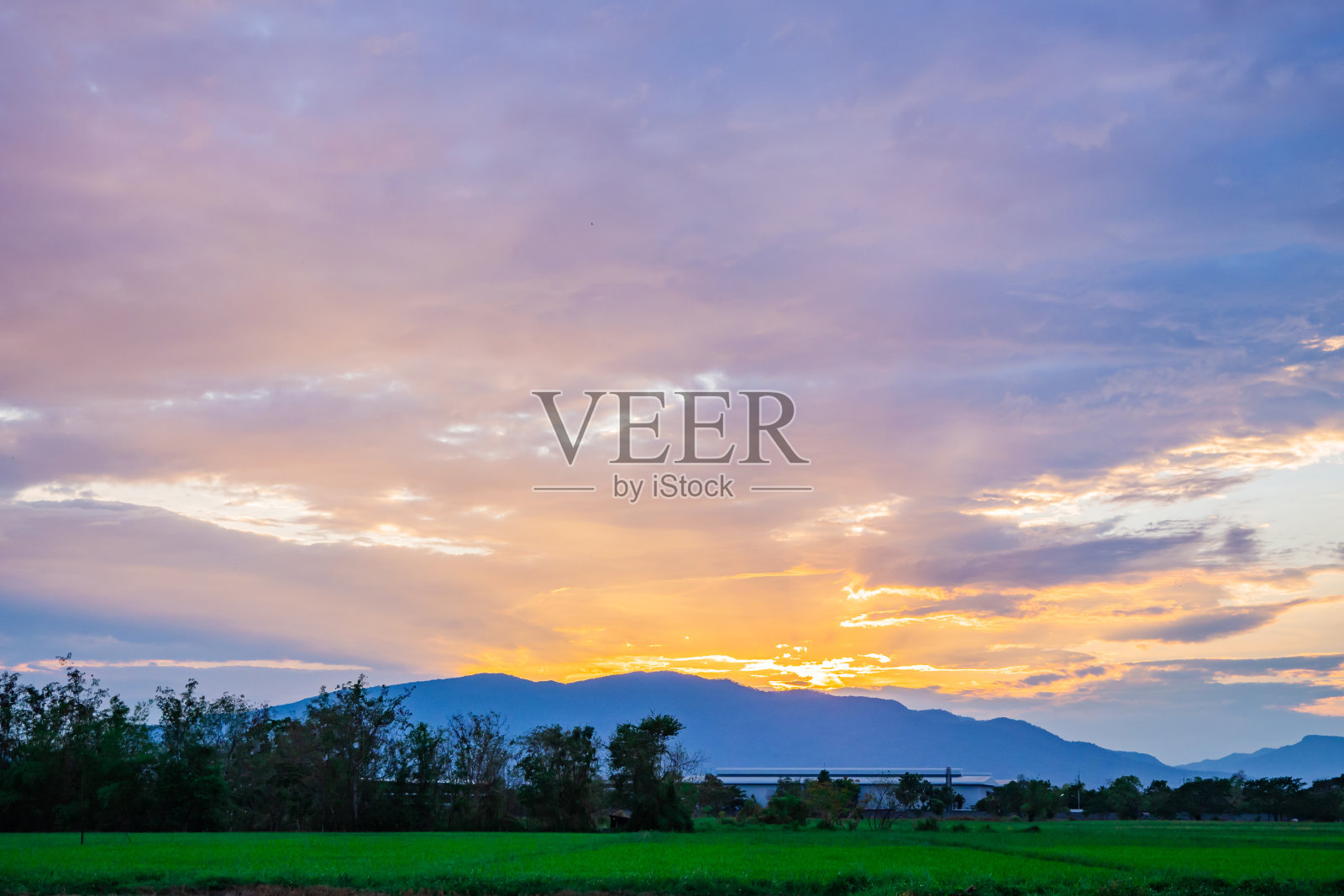 美丽的温暖多彩的日出或惊人的日落在一个大的山，与绿色的稻田风景在夏季农业时间，亚洲县，或农业农村。景观背景纹理。照片摄影图片