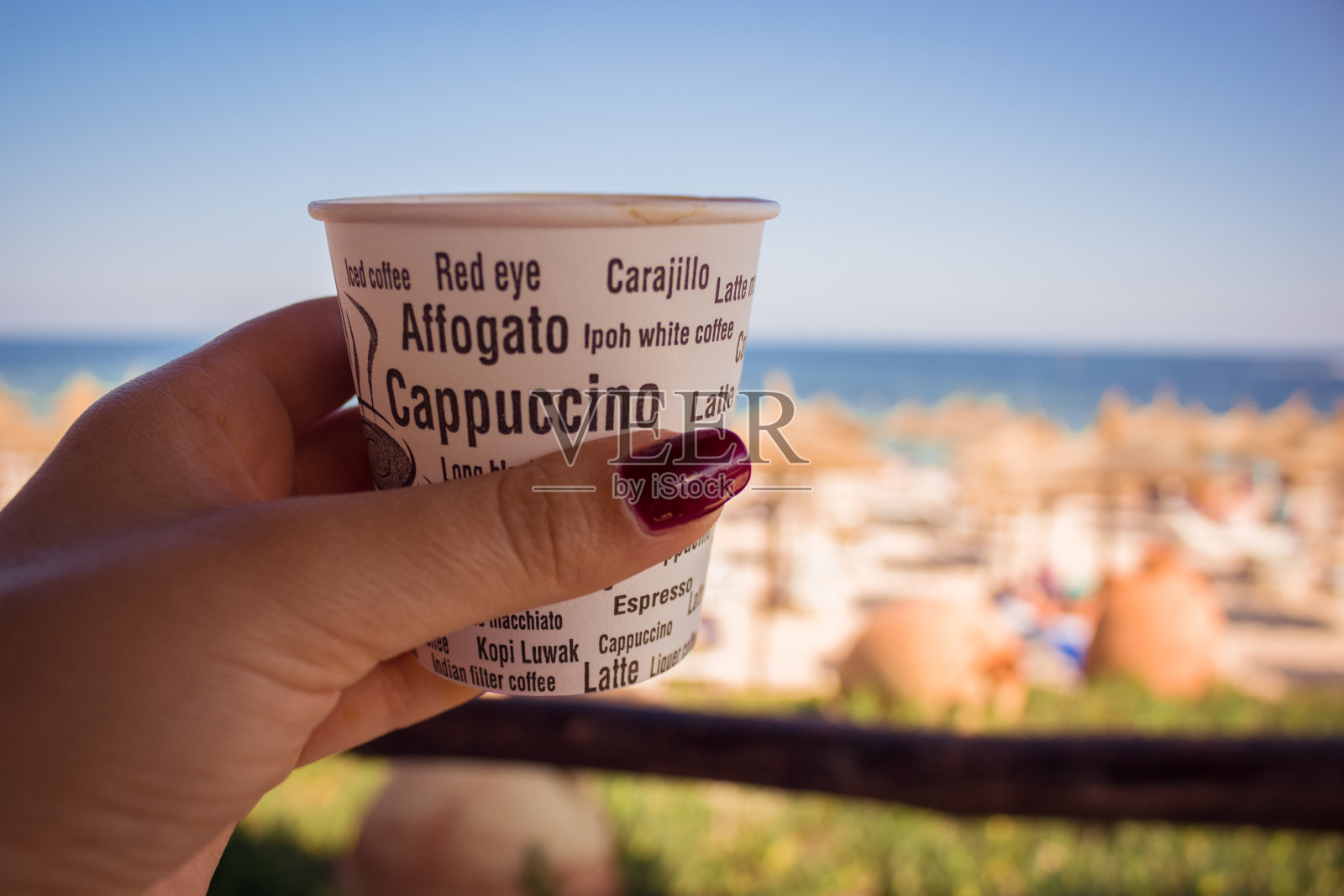 手捧一杯咖啡，面前是一片蔚蓝的大海。照片摄影图片