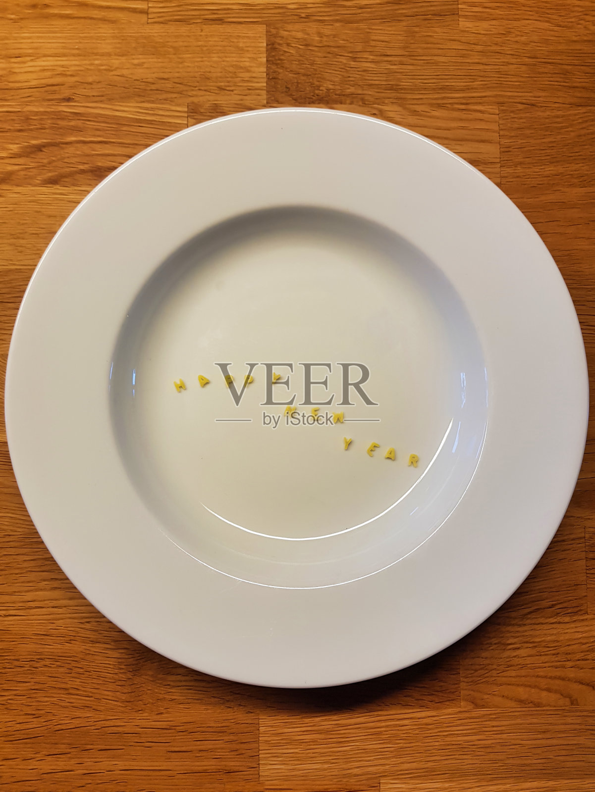 “新年快乐”由可食用的字母组成。以木为背景的盘子上的字母形式的意大利面。照片摄影图片