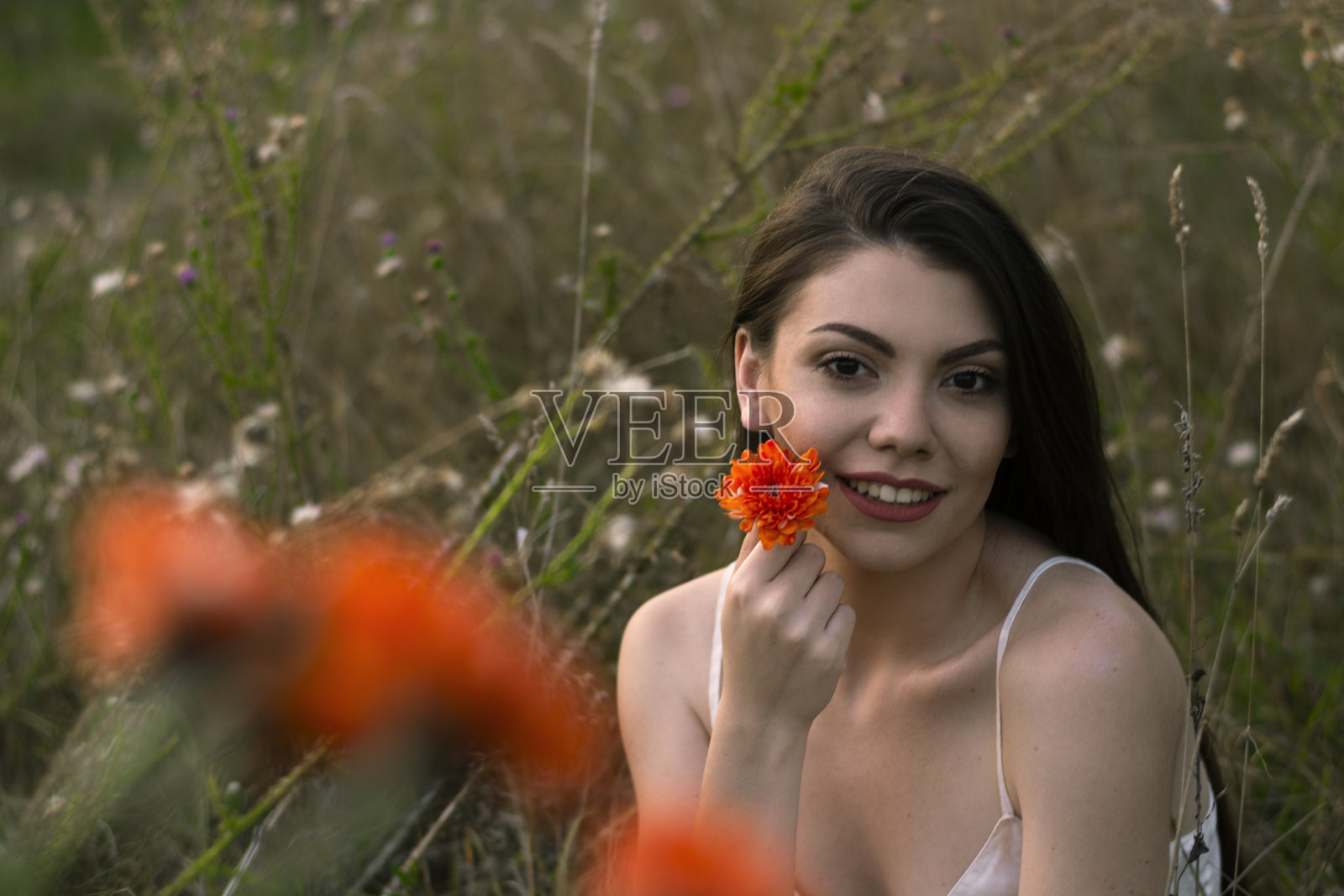 草地上有个美丽的女孩，手里拿着一朵桔黄色的花。照片摄影图片