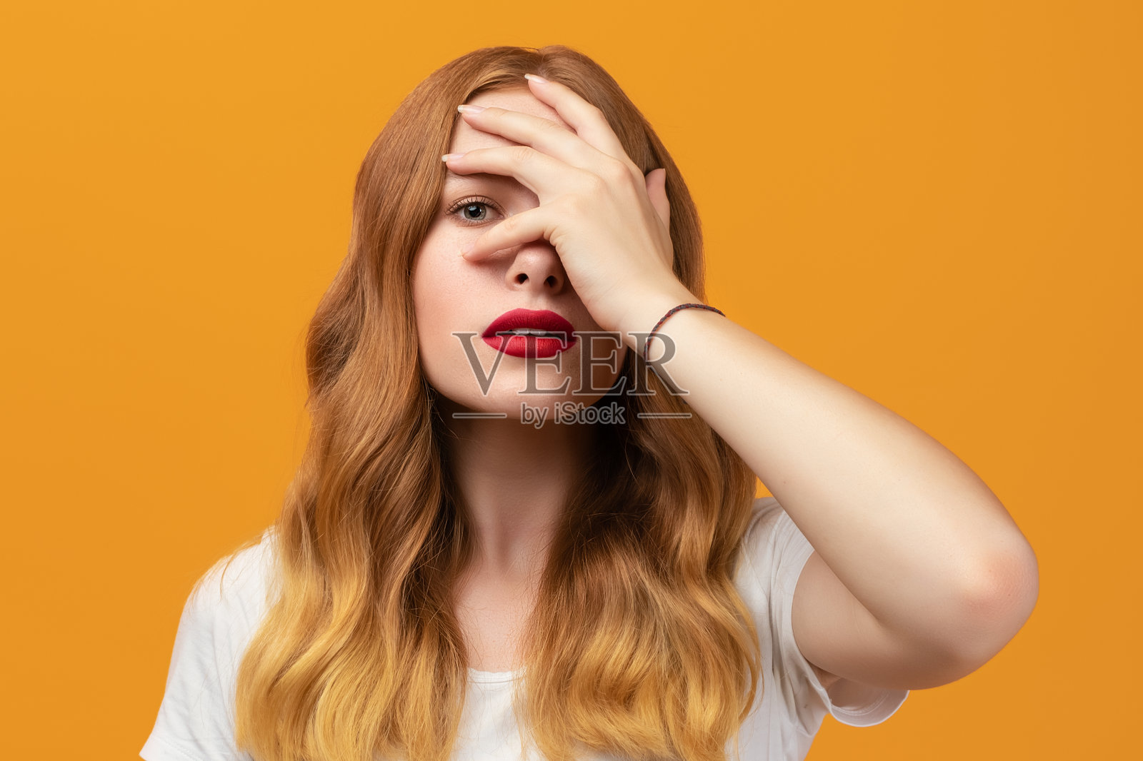 漂亮的女孩，一头金色的长发，从手指间看过去，表情尴尬照片摄影图片