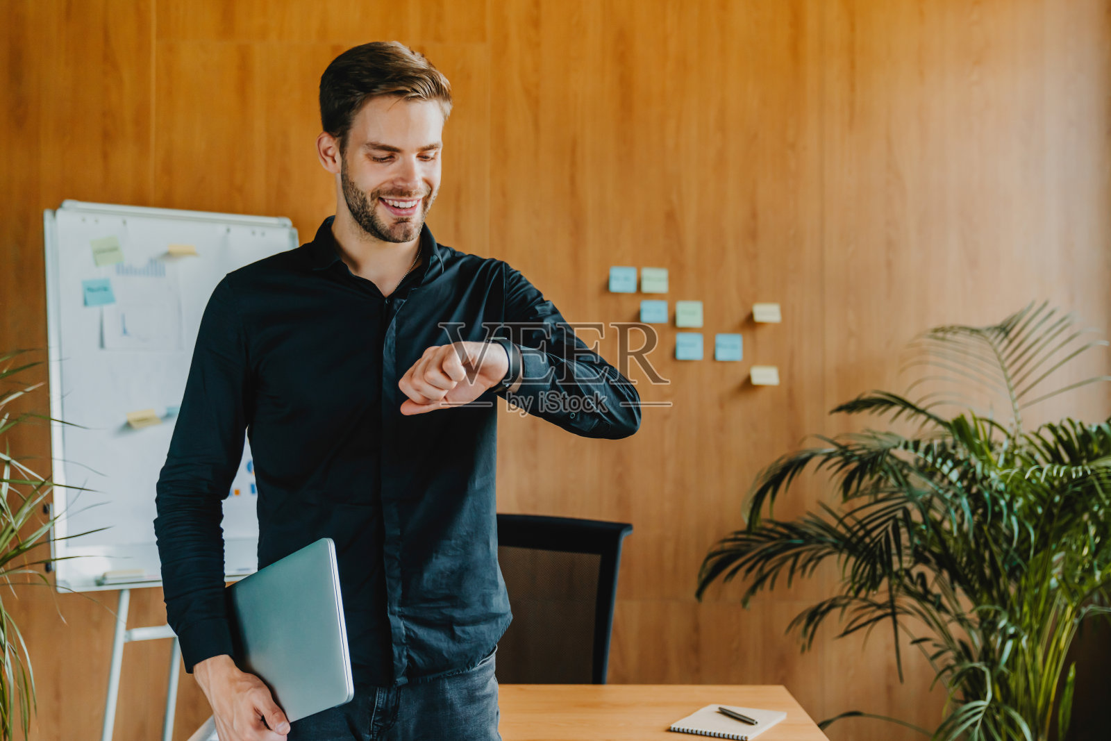 在创意办公室里拿着笔记本电脑看手表的商人照片摄影图片