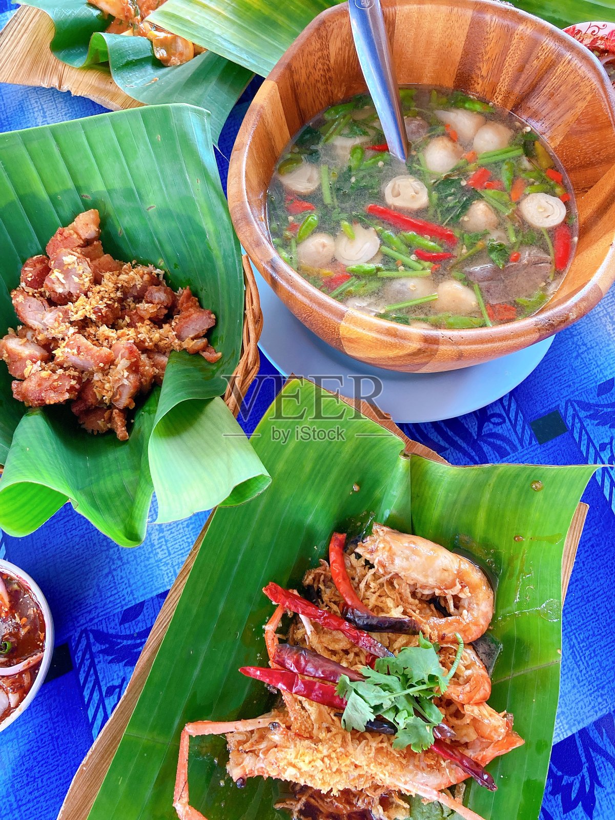 桌上摆着泰国菜，木碗冬阴功，香蕉叶盘蒜炸虾，蒜炸猪肉照片摄影图片