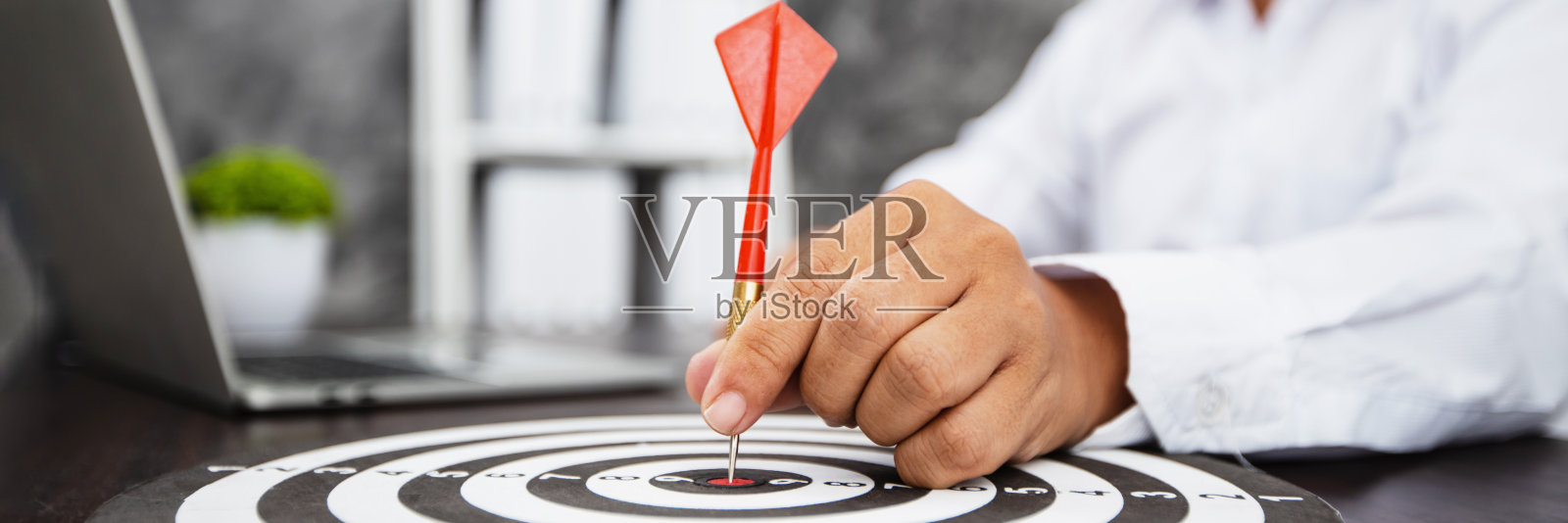 手握飞镖的商人将目标对准成功的目标放在桌上，成功与成就，赢家与赢家的概念照片摄影图片
