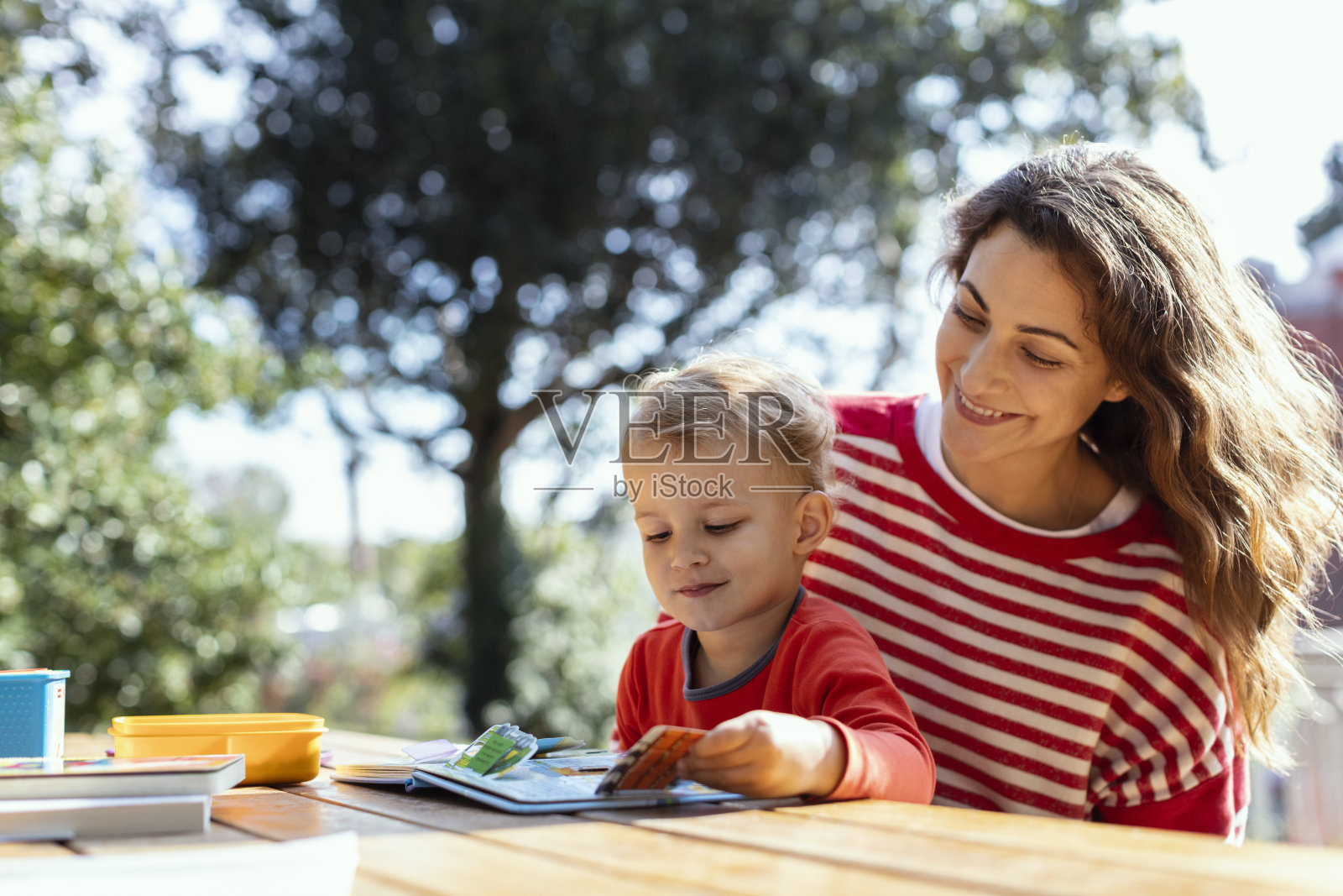 快乐的母亲和蹒跚学步的孩子在花园里读掀瓣儿童书照片摄影图片