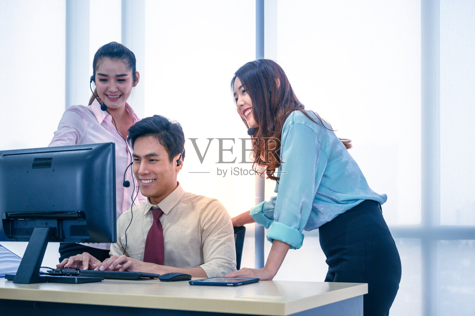 一群年轻的商务团队，戴着耳机和电脑在办公室工作。照片摄影图片