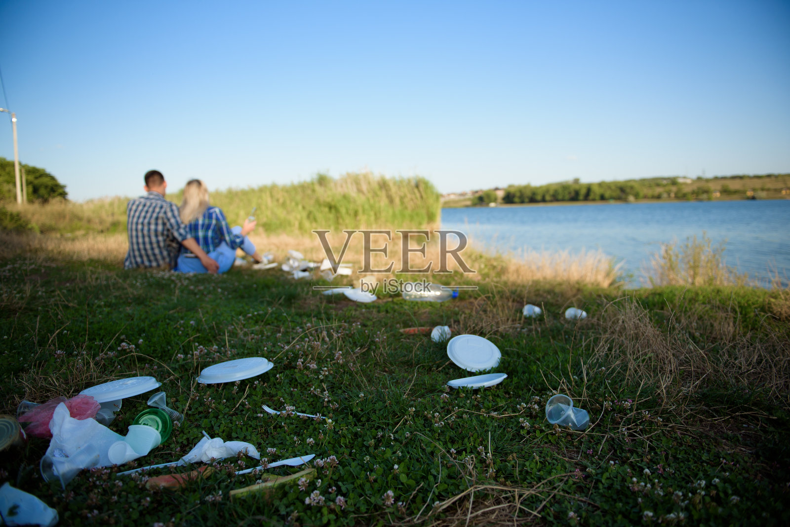 海滩上的垃圾。一对年轻夫妇在海滩上休息，旁边是一堆垃圾。人与自然概念照片摄影图片