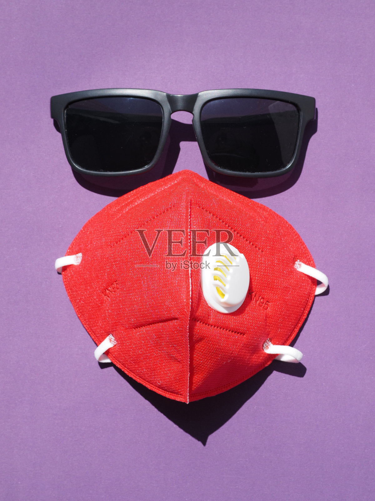 红色KN95防护口罩，黑色太阳镜，紫色背景。照片摄影图片