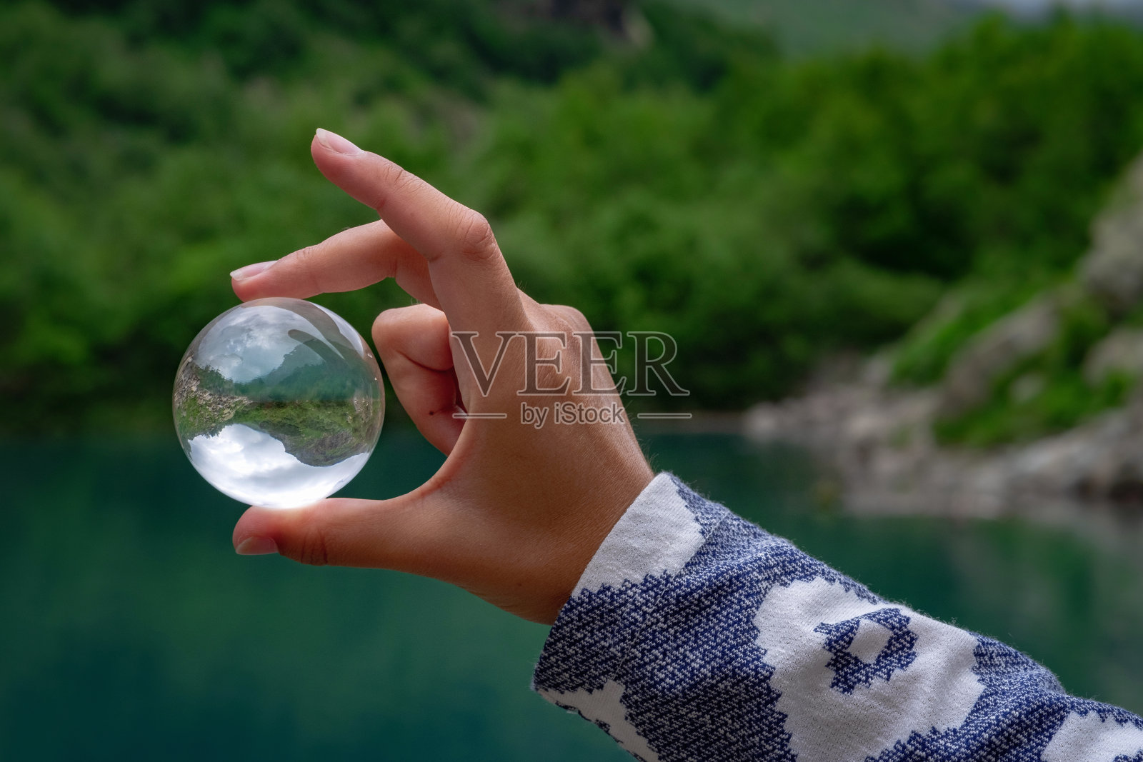 一个女人的手拿着一个球形的玻璃球，背景是一个美丽的山湖。照片摄影图片