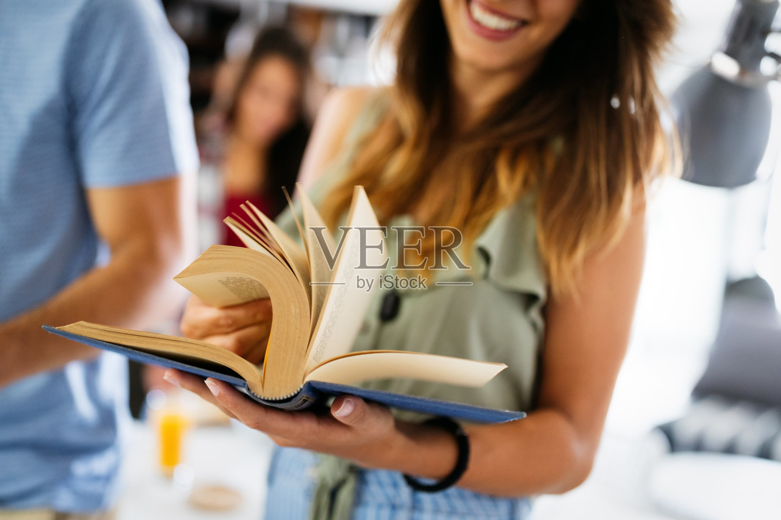 美丽快乐的女人拿着书，笑着和他的朋友在后面聊天照片摄影图片