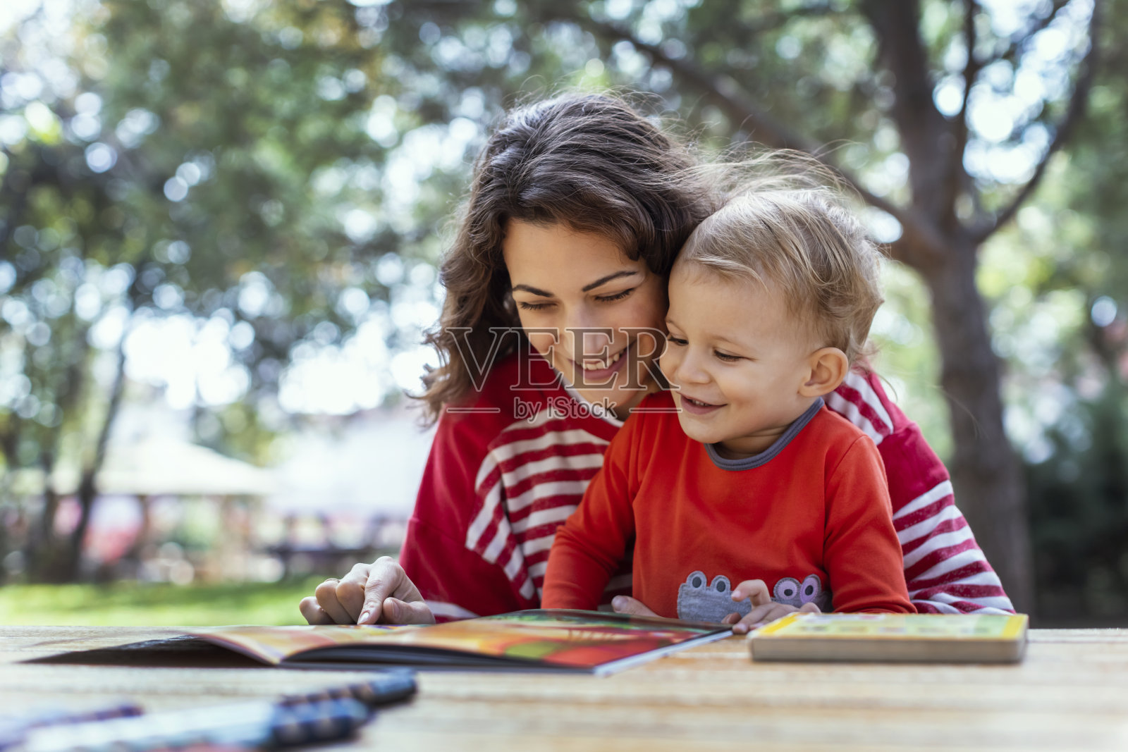母子俩在花园里看书，野餐桌上放着蜡笔照片摄影图片