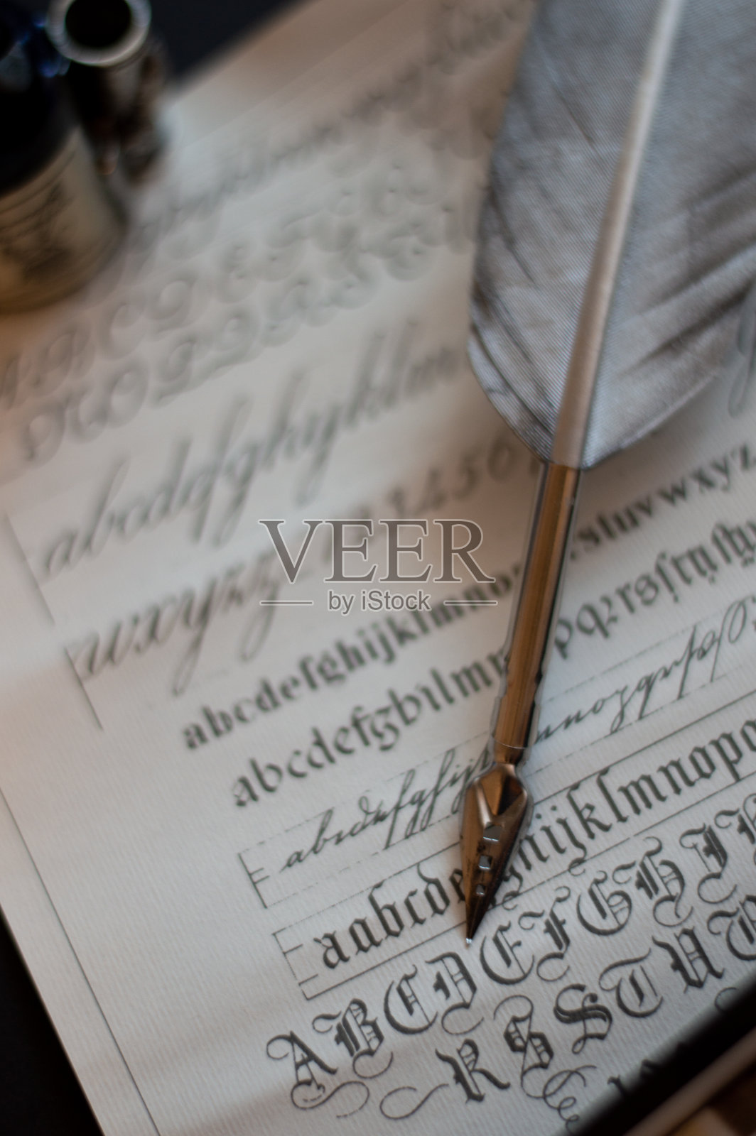 一张带有旧墨水瓶的钢笔照片，在纸莎草纸上有几个不同形状的笔尖和书法例子。照片摄影图片