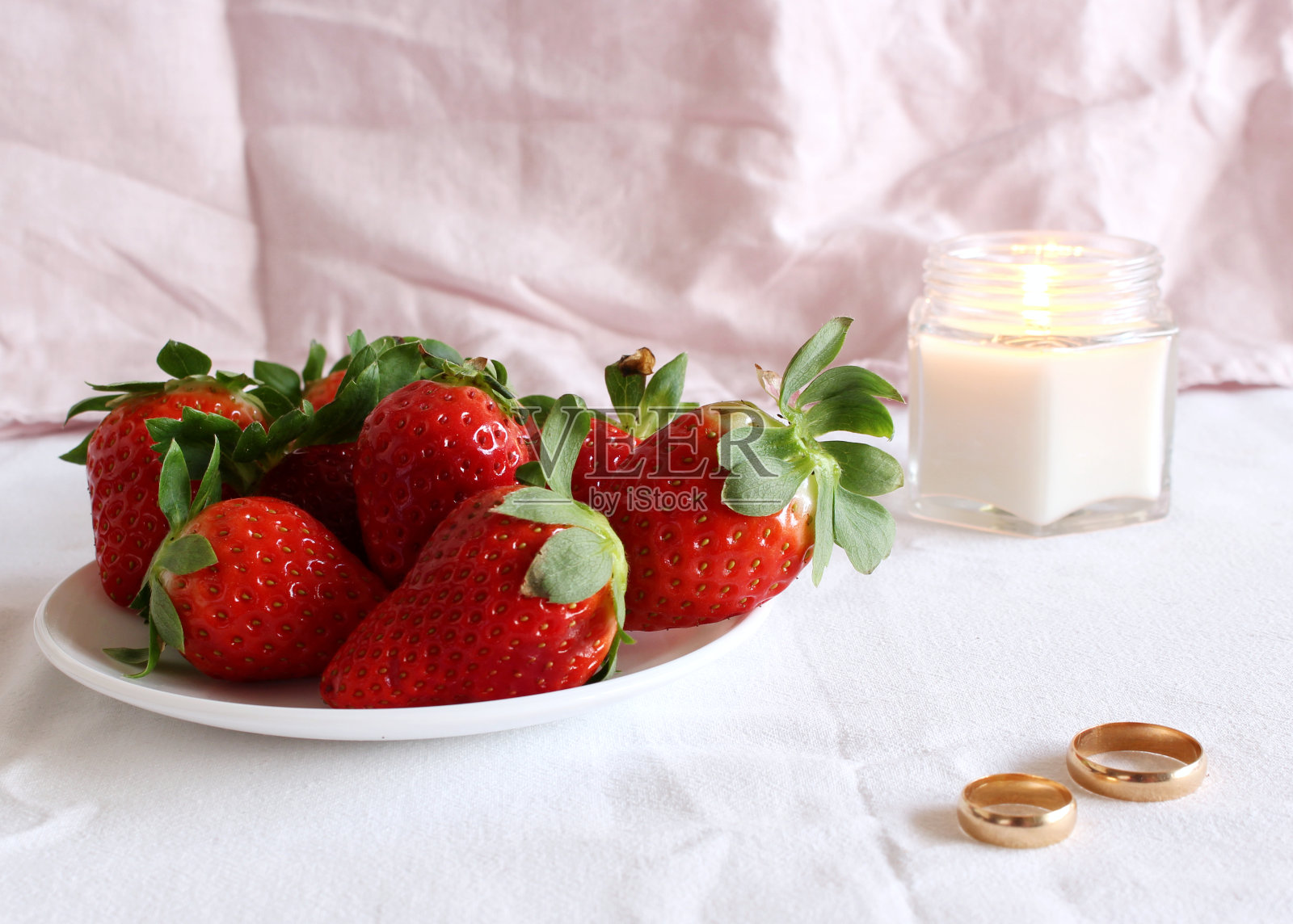 明亮的婚礼场景，瓷盘上的新鲜草莓和婚礼戒指的白色背景。女性风格的库存照片。照片摄影图片