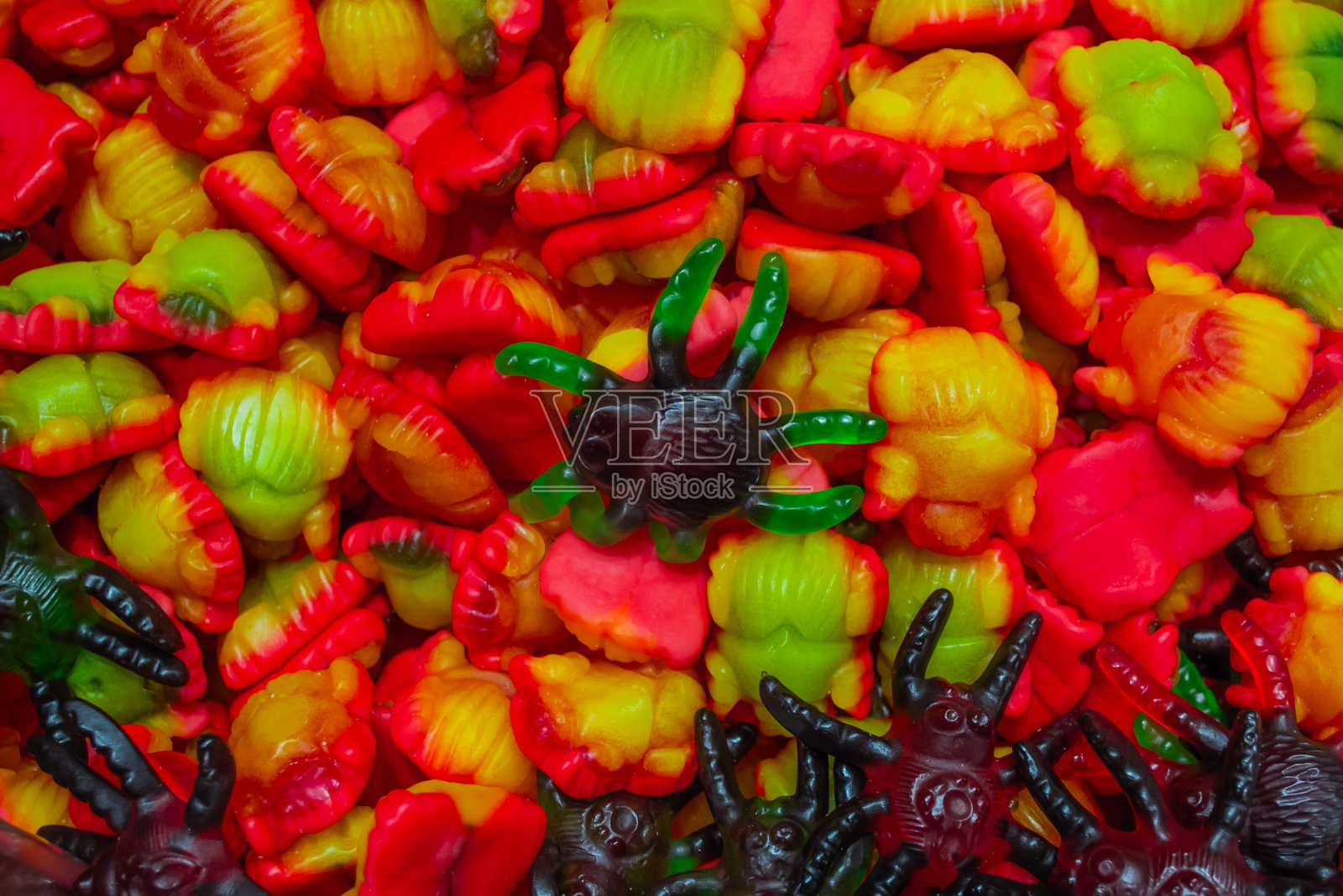 一堆软糖，形状像红黄相间的圣甲虫和绿红相间的黑蜘蛛。万圣节的概念，不给糖就捣蛋。甜蜜的背景照片摄影图片