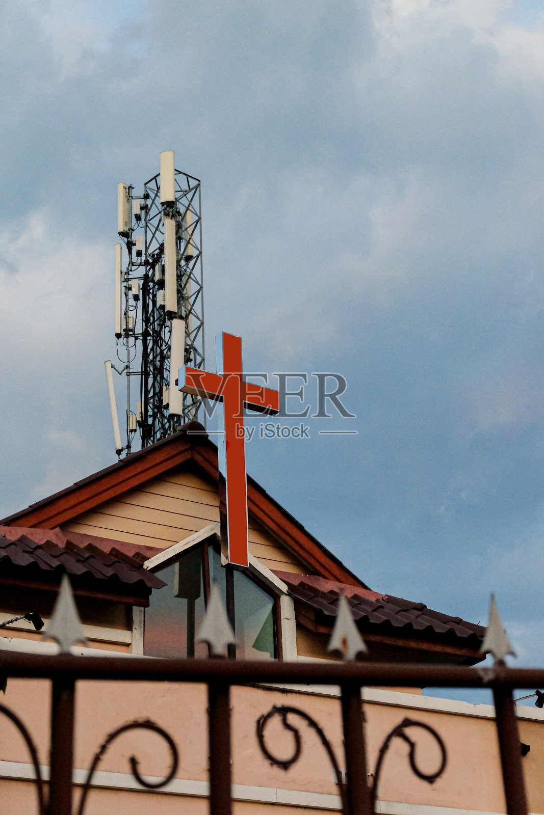教堂顶上有红十字，还有电信塔。照片摄影图片