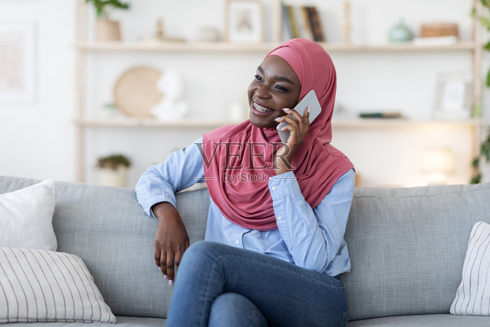 年轻的黑人穆斯林妇女戴着头巾在家打电话照片摄影图片