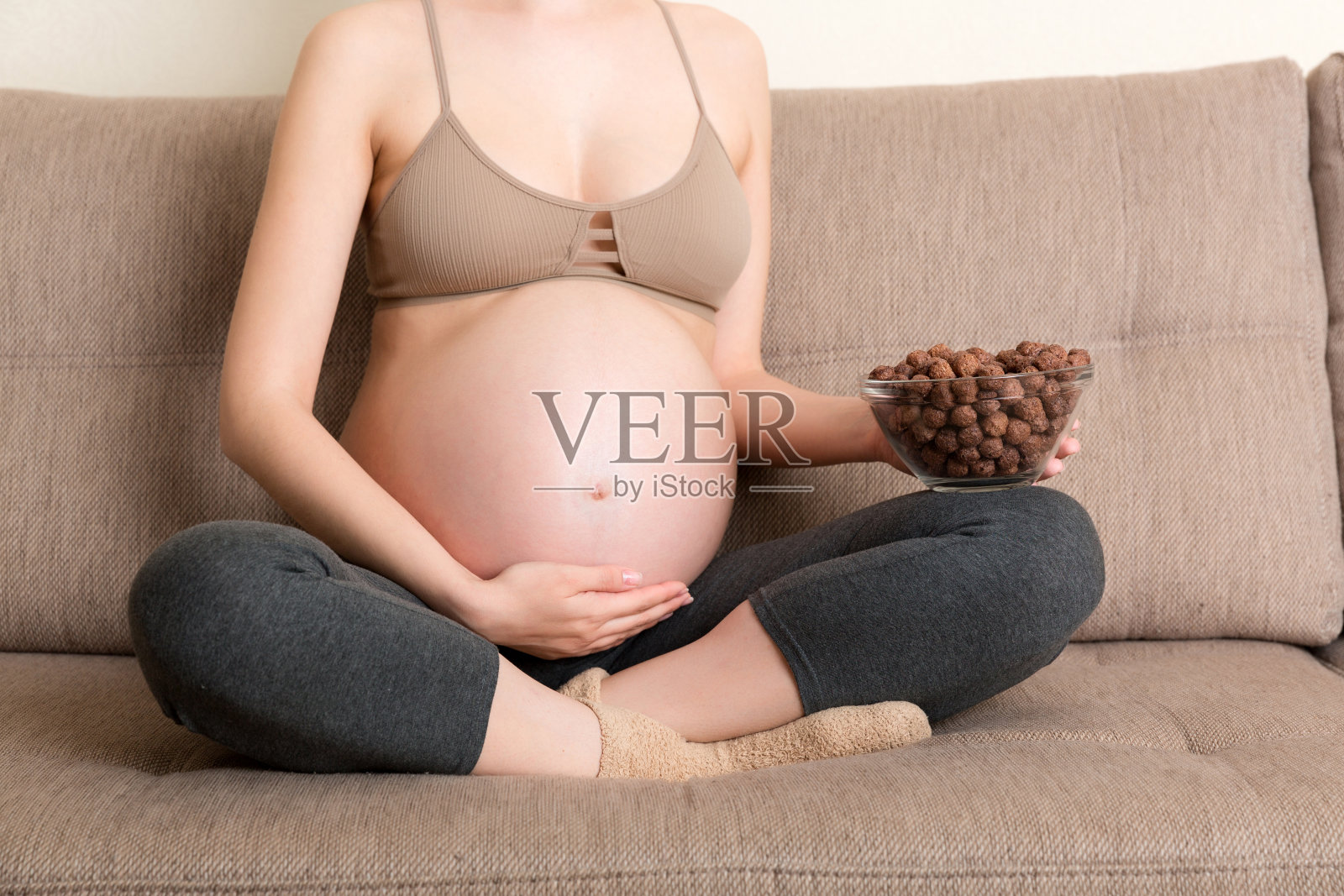 近距离的孕妇正在吃松脆的巧克力麦片球碗休息在沙发上。享受怀孕期间的食物概念照片摄影图片
