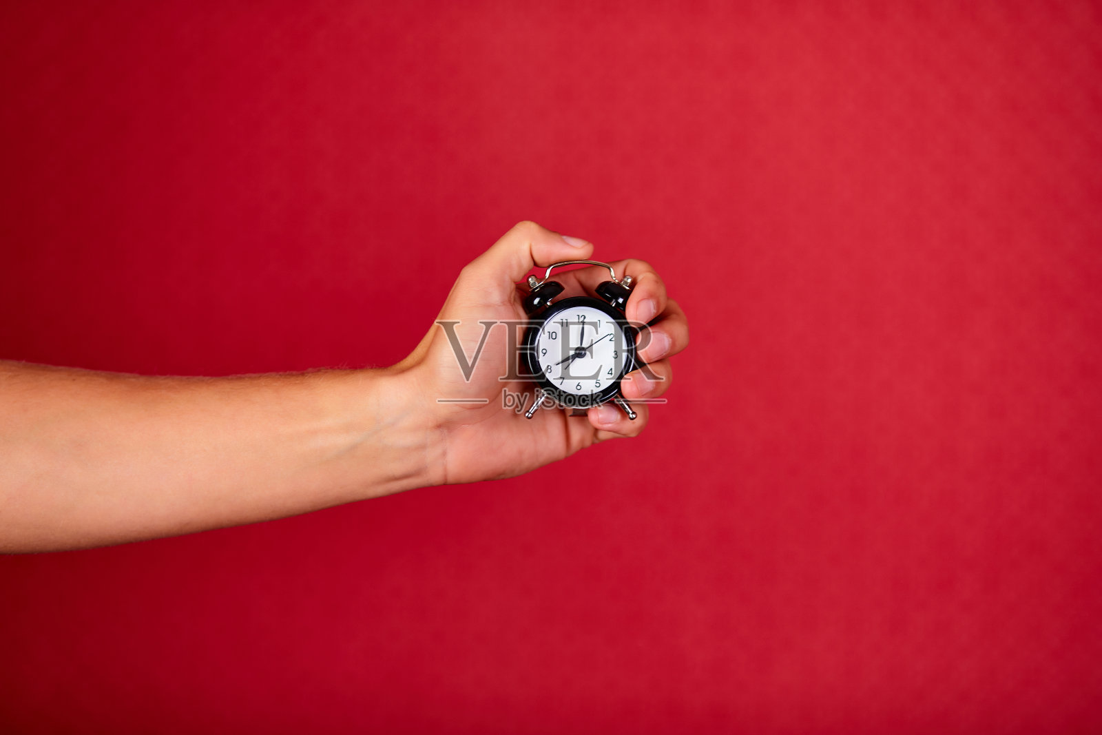 在红色演播室背景上，一名男子一手拿着黑色闹钟照片摄影图片