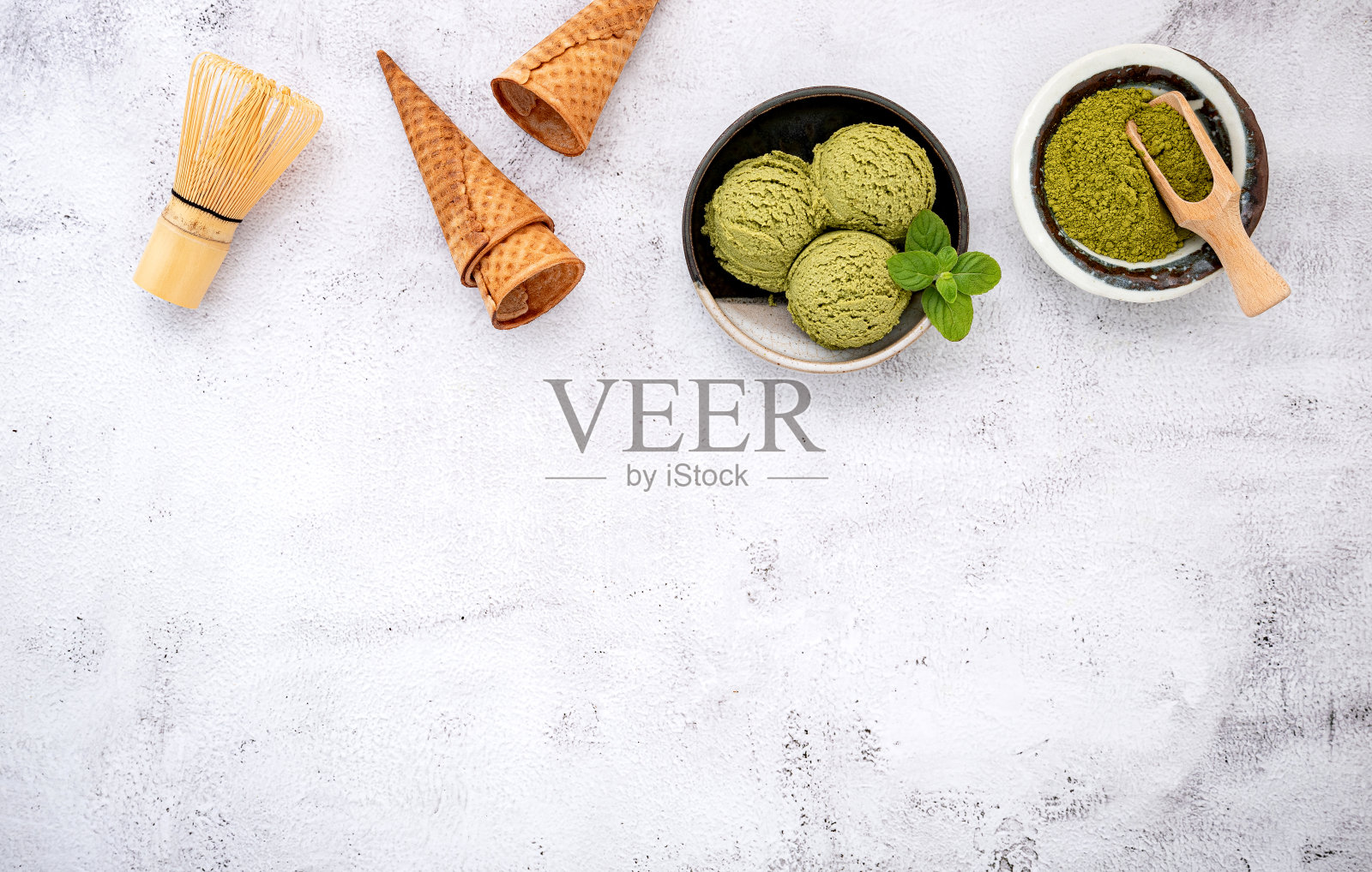 抹茶绿茶冰淇淋与华夫蛋筒和薄荷叶设置在白石背景。夏季和甜蜜的菜单概念。照片摄影图片