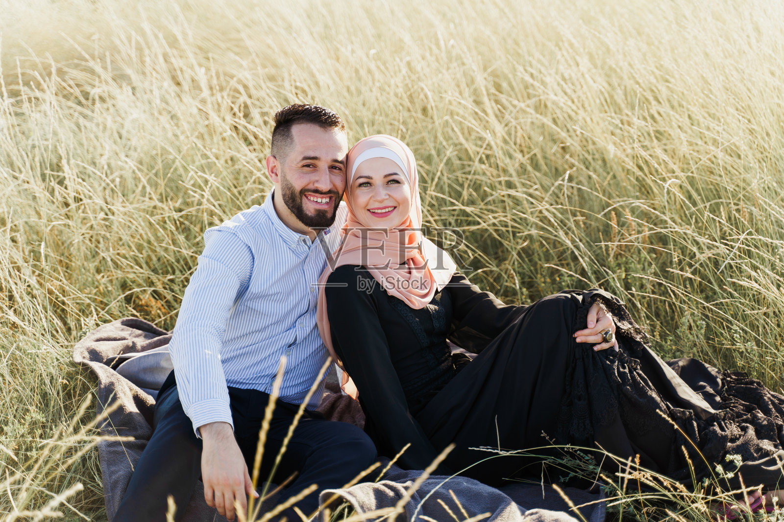 穆斯林的爱情故事。草地上的混合座位，微笑和拥抱。戴着头巾的女人看着她的男人。为网上约会机构做广告照片摄影图片