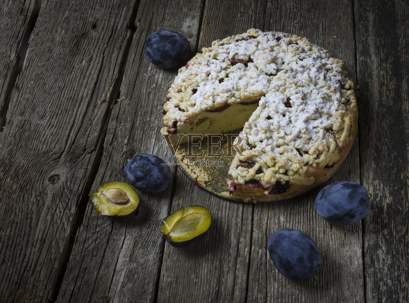黑色木制背景上的乡村李子蛋糕。旧桌子上放着圆圆的李子馅饼。照片摄影图片