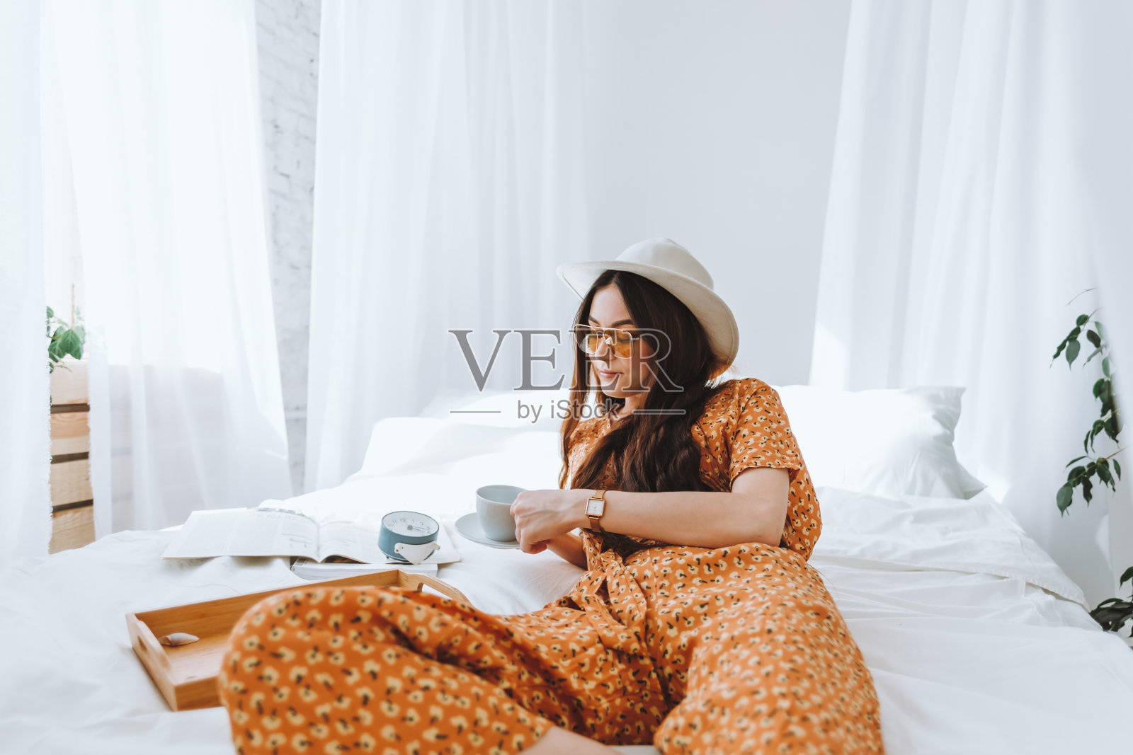 年轻时尚的女人戴着眼镜和白帽子躺在床上喝咖啡照片摄影图片