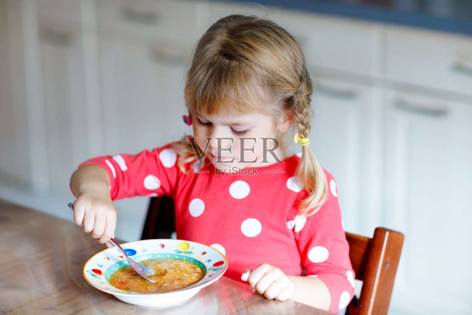 可爱的小蹒跚学步的女孩在厨房吃新鲜煮熟的蔬菜汤。快乐的孩子午餐或晚餐吃健康的食物。孩子学习。家庭，托儿所，幼儿园或日托所照片摄影图片