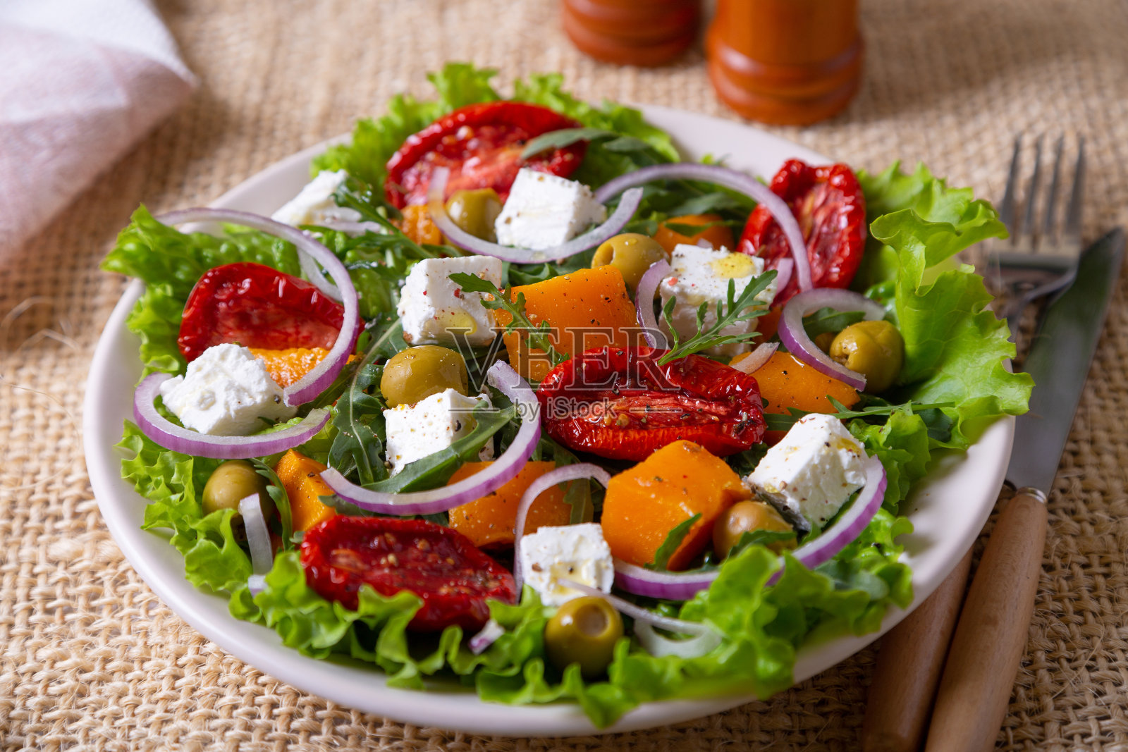 热沙拉配南瓜，羊乳酪，番茄干，橄榄，芝麻菜和红洋葱。照片摄影图片