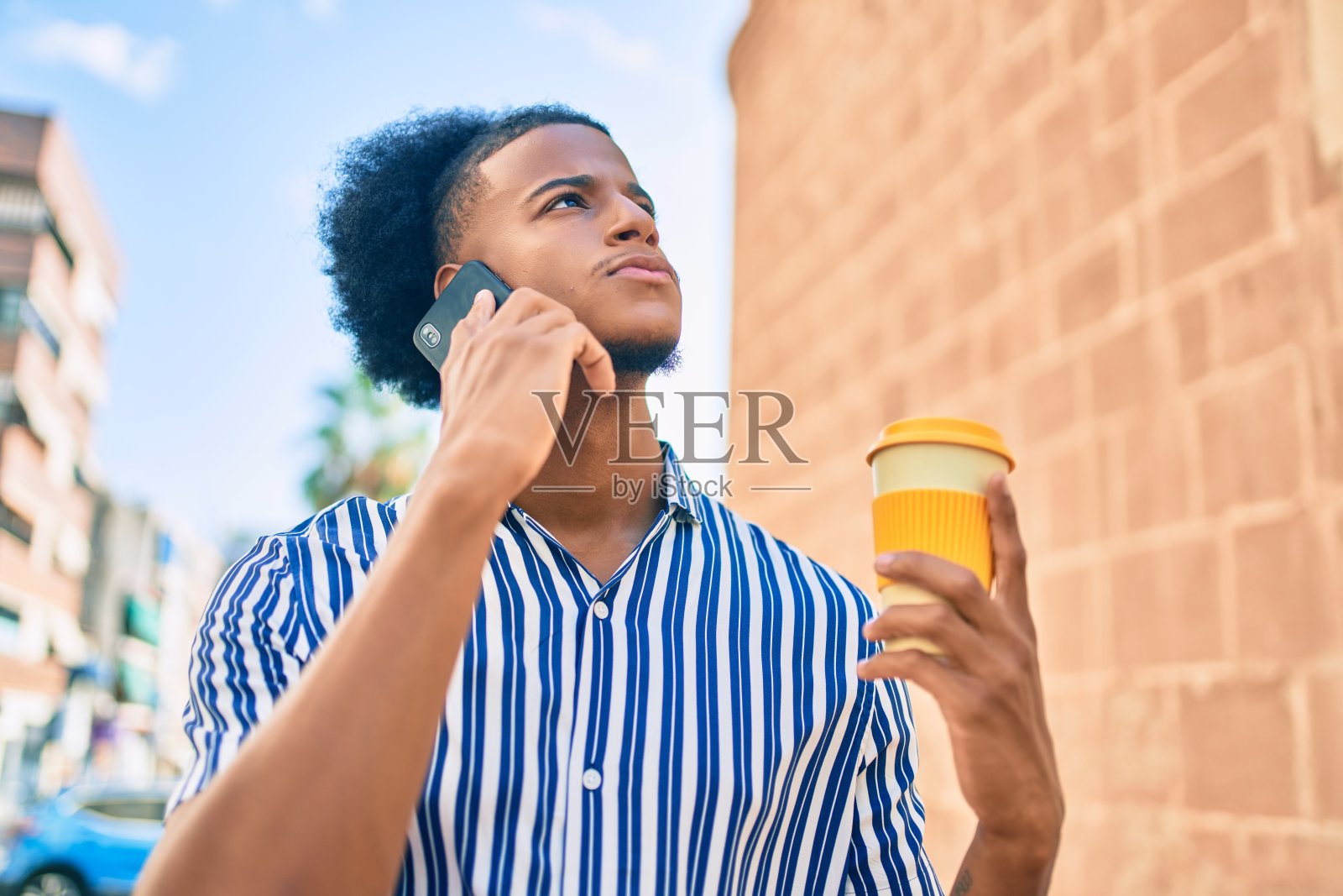 年轻的非洲裔美国人与不愉快的表情在智能手机上交谈和喝咖啡的城市。照片摄影图片