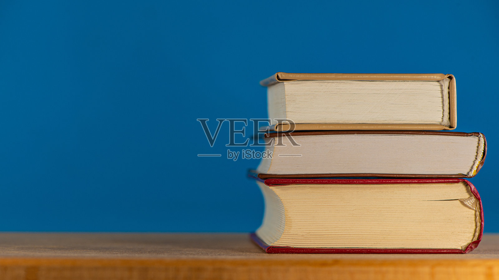 蓝色背景的橡木桌子上放着三本书。照片摄影图片