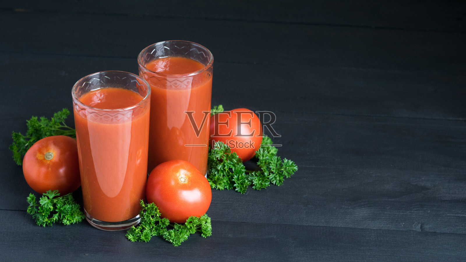 两杯新鲜的番茄汁，红色成熟的西红柿和欧芹在黑色的木头背景。有选择性的重点,copyspace照片摄影图片