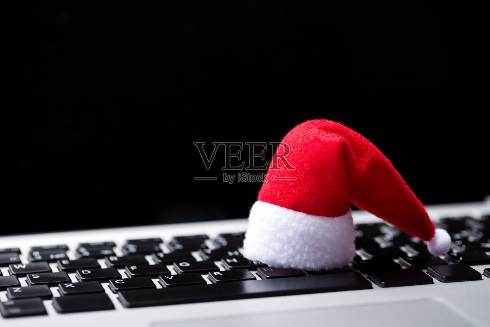 圣诞老人帽在笔记本电脑键盘上。正在网上搜索庆祝圣诞的地点照片摄影图片