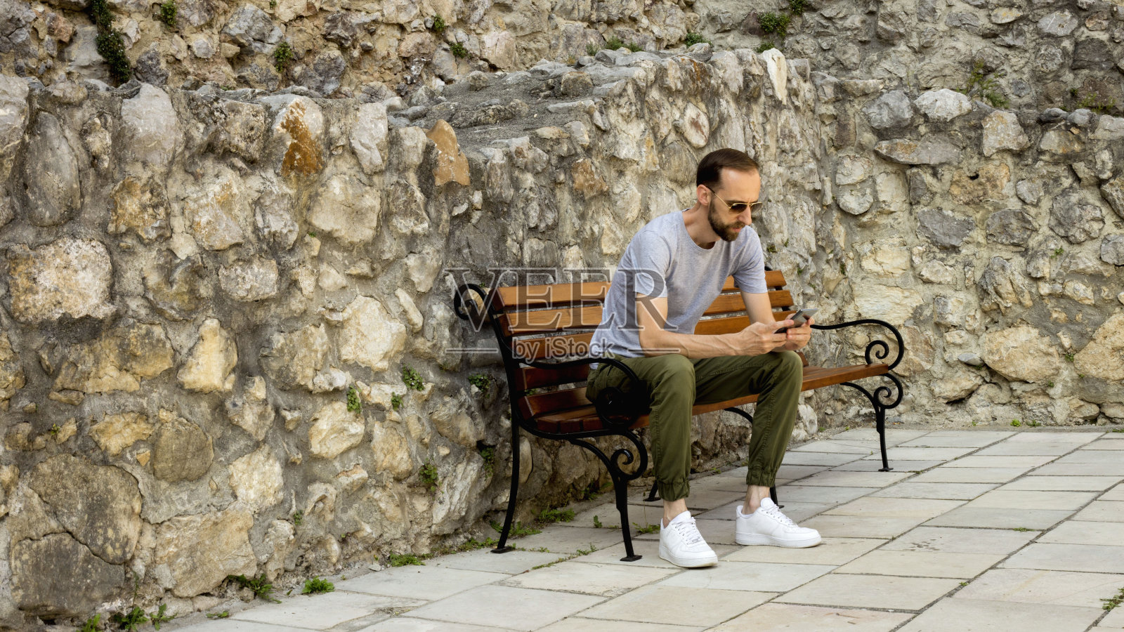 夏天的一天，一个戴着太阳镜的年轻人坐在外面的长凳上。照片摄影图片